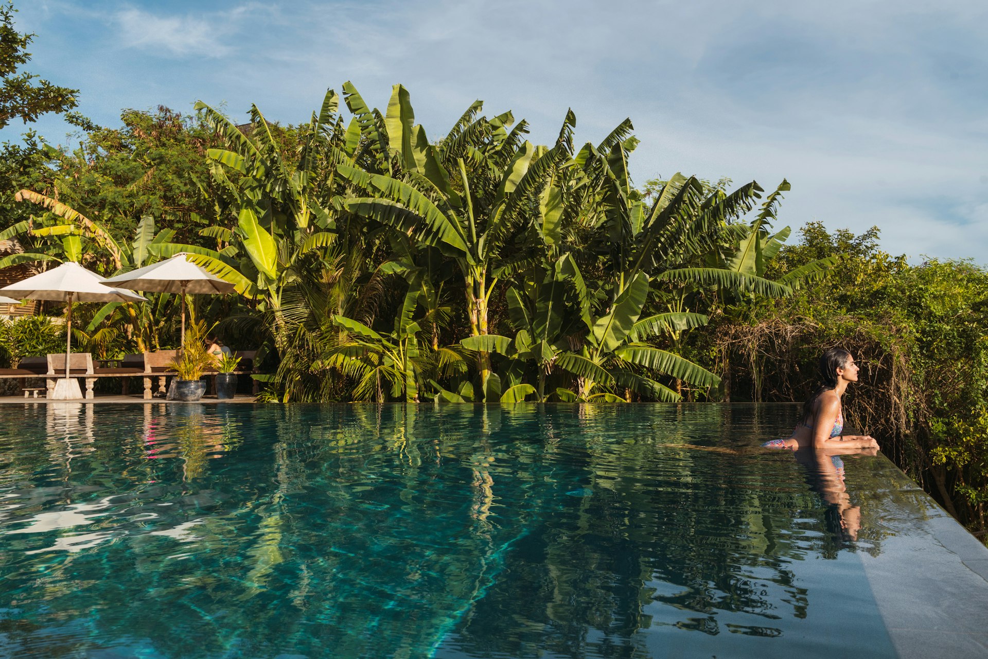 Horizontal panoramic view of woman resting at paradisiacal infinite pool resort with palm trees in Lombok island
