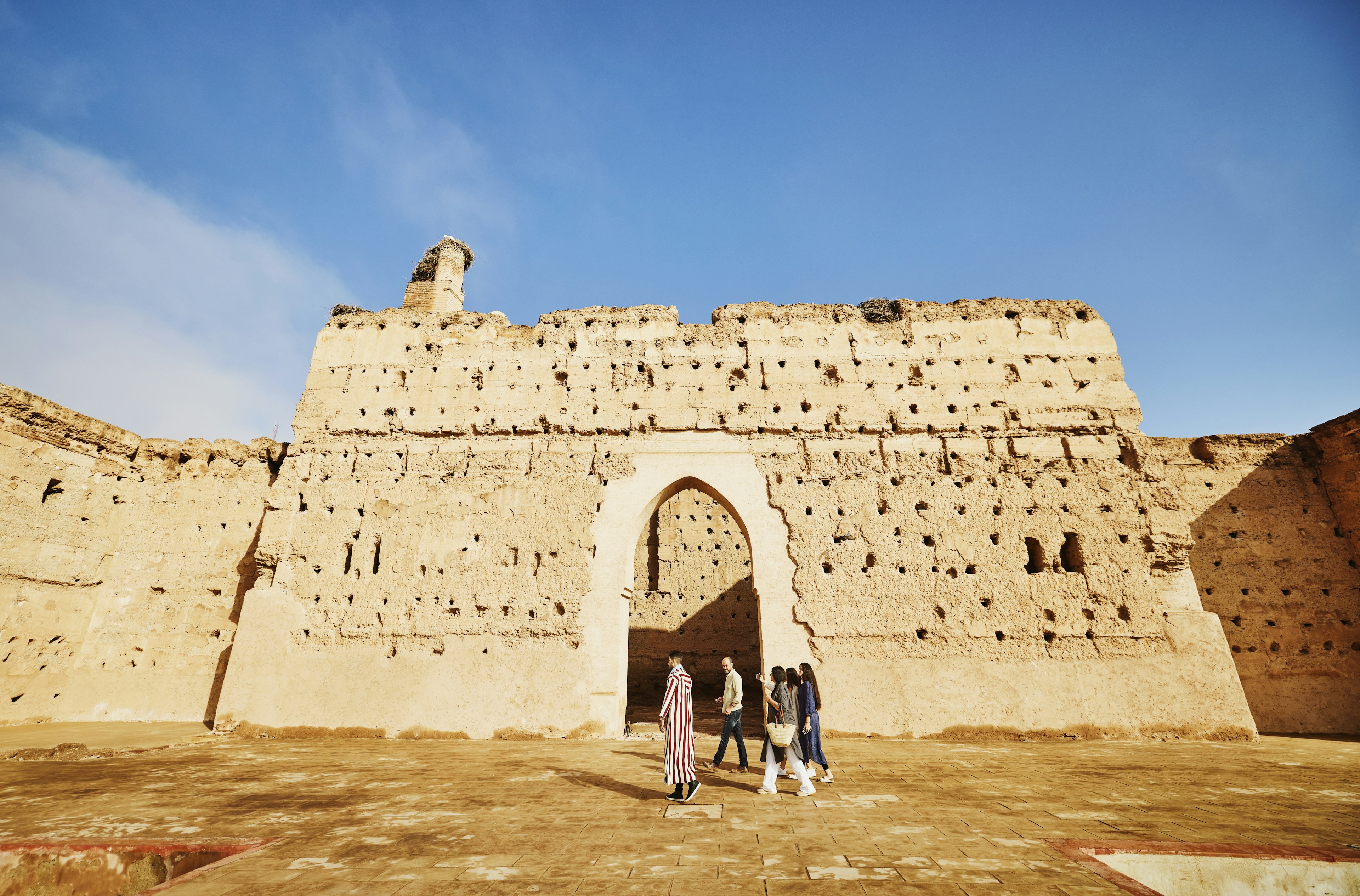 A group walks in front of a terra-cotta-colored palace in Marrakesh