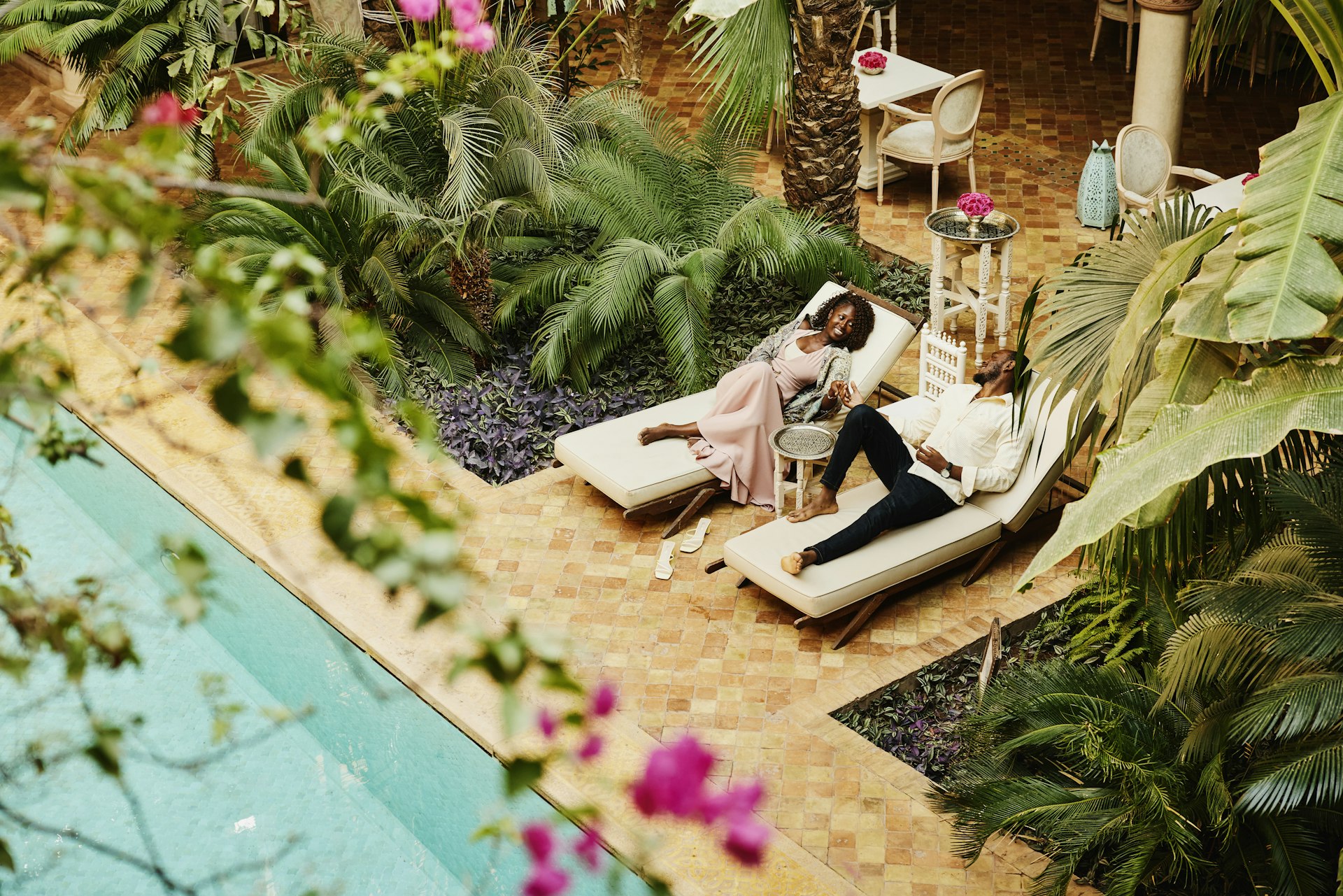 Wide high angle shot of couple relaxing in lounge chairs by pool in courtyard of luxury hotel while on vacation