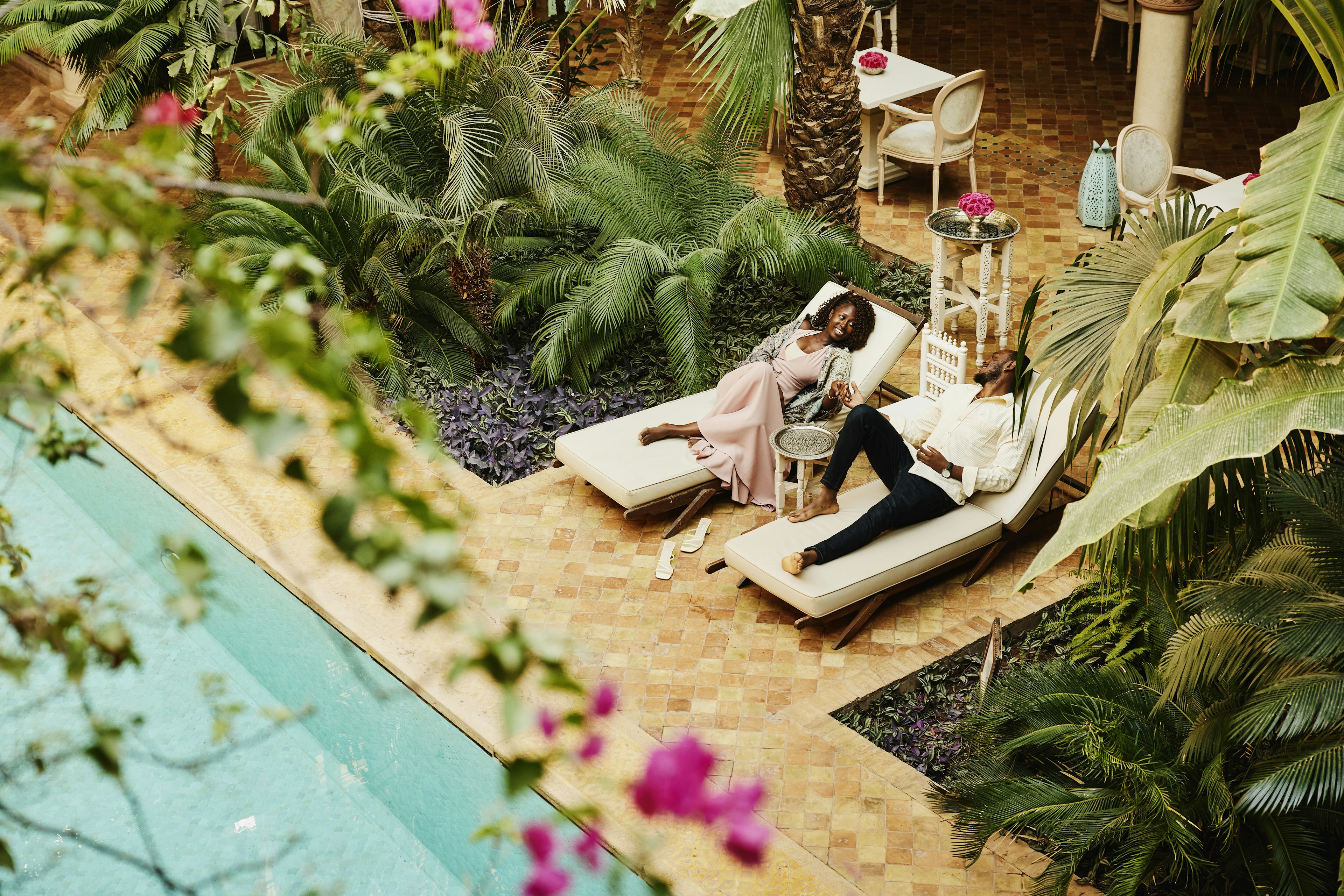 Wide high angle shot of couple relaxing in lounge chairs by pool in courtyard of luxury hotel while on vacation