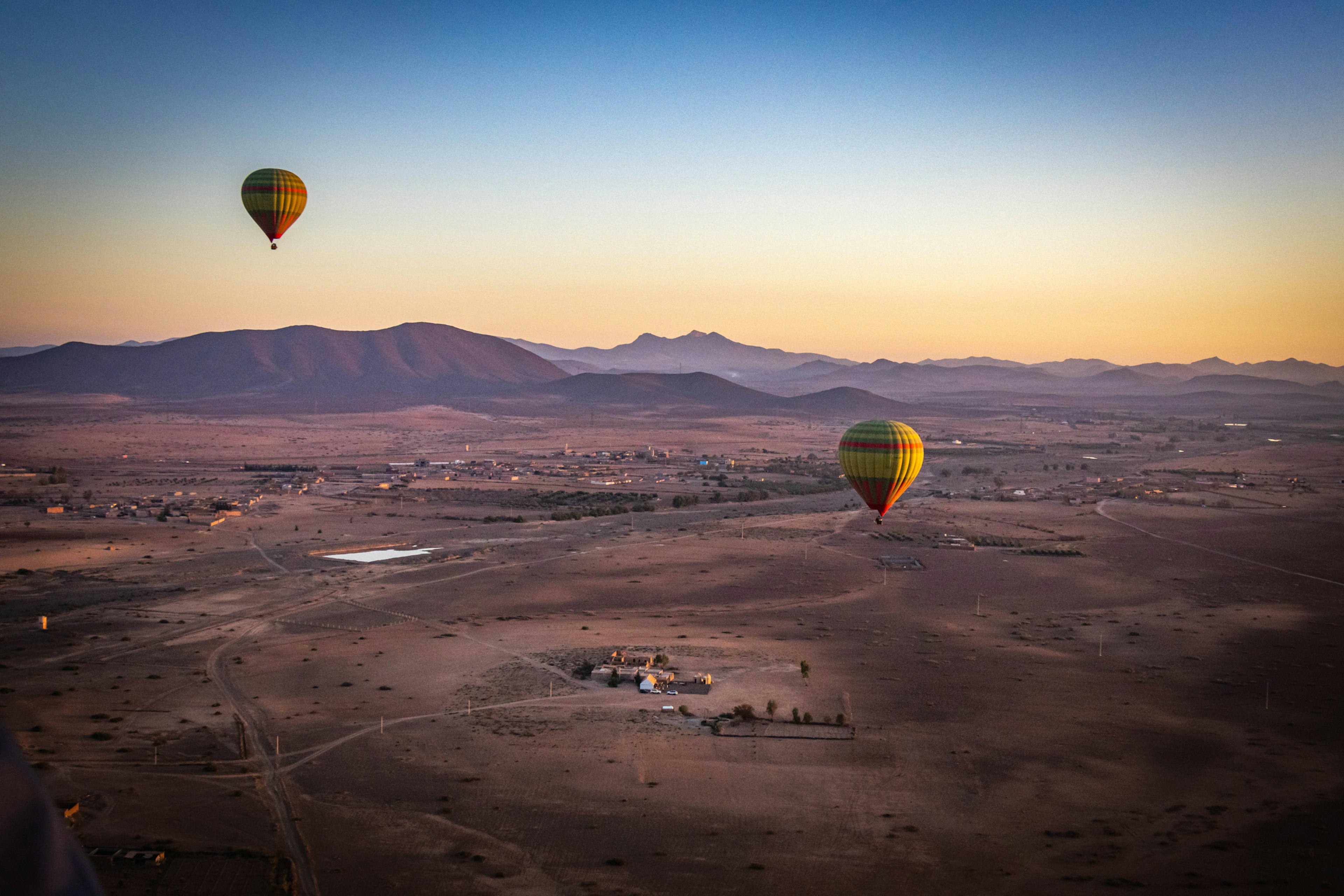 Hot-air balloons take off over a red-hued landscape as the sun rises