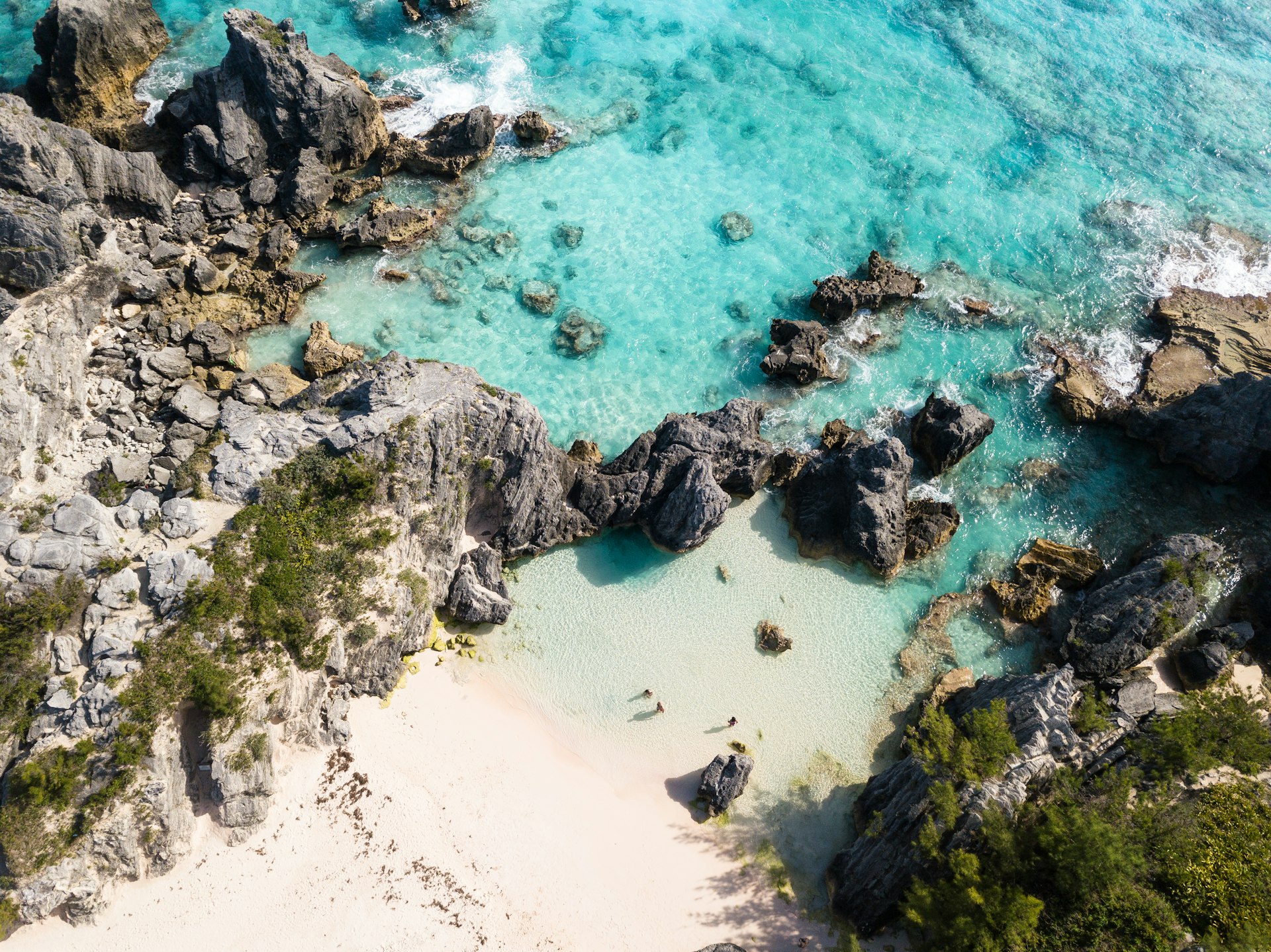 Aerial view of a rocky cove in Bermuda with two people standing on the shore