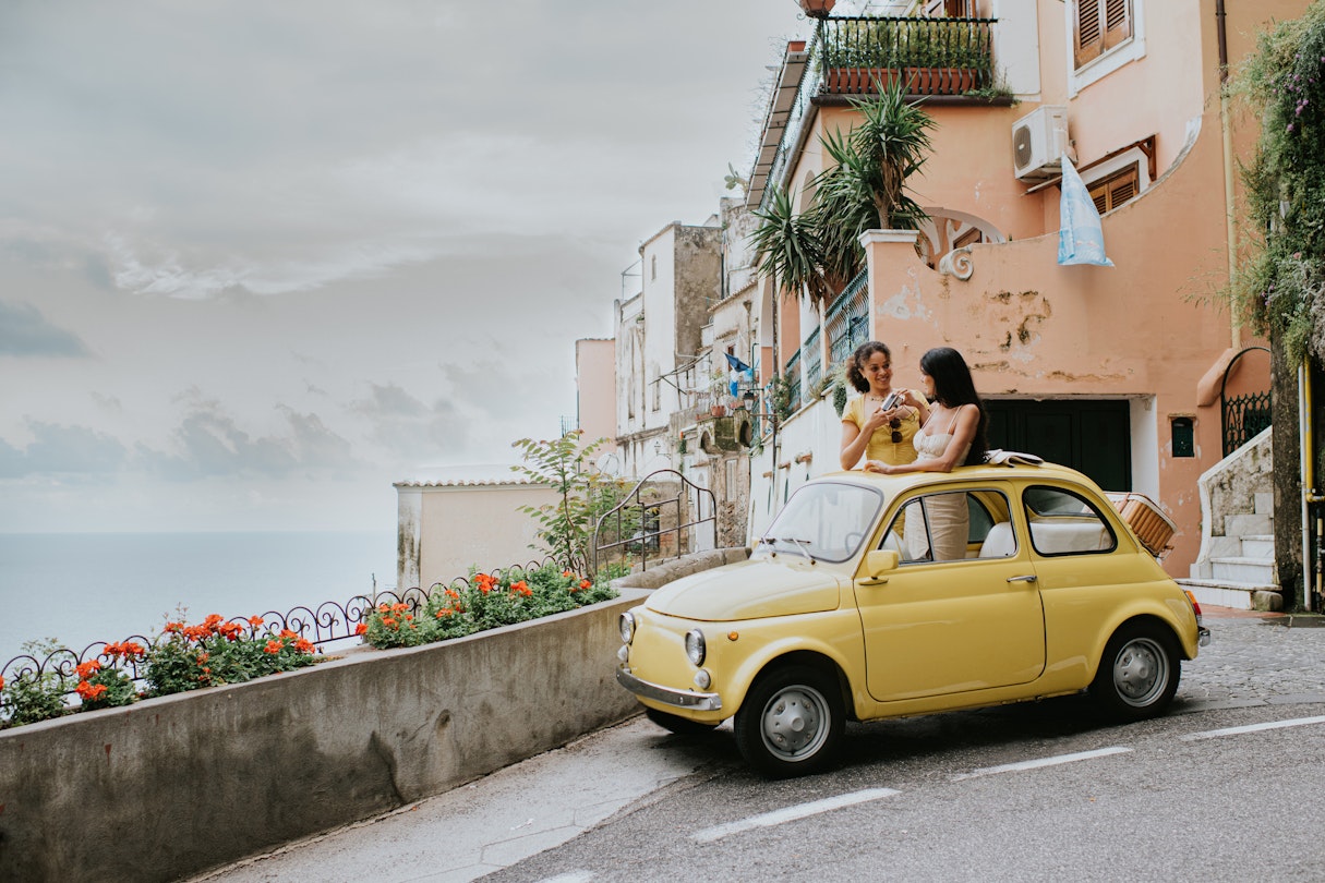 Two beautiful young woman inside a small, vintage yellow car. The top remains open. They stand up in the vehicle, through the sunroof and take photos of each other. We can see Italy's famous view of Positano in the background. Depicts a scene of experiential travel, suggesting renting a car, travel tours, European road trips and nostalgia.
1492413341