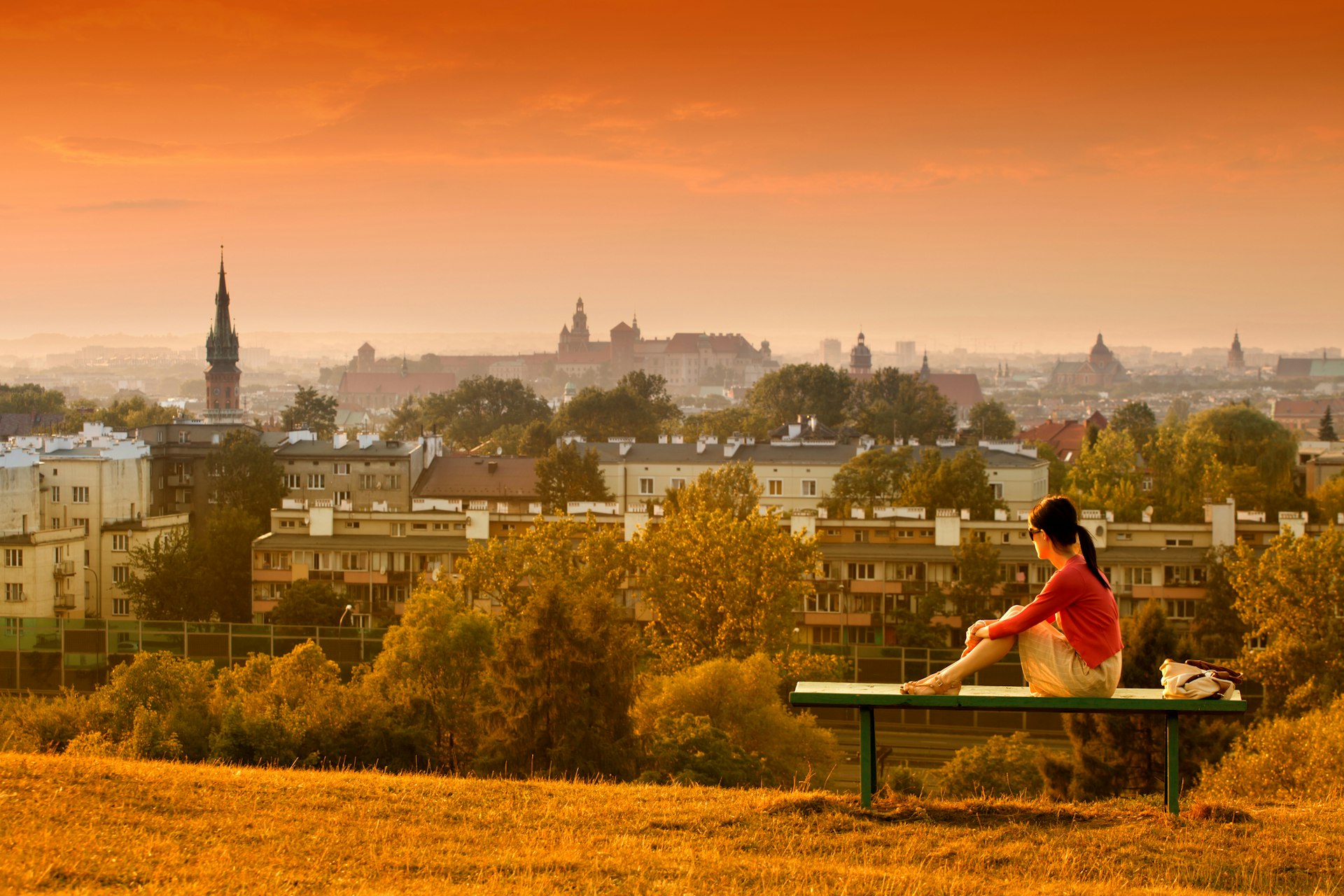 Young girl having a relax moment on top of the Kraków Mounds, looking out at the Kraków skyline at dusk