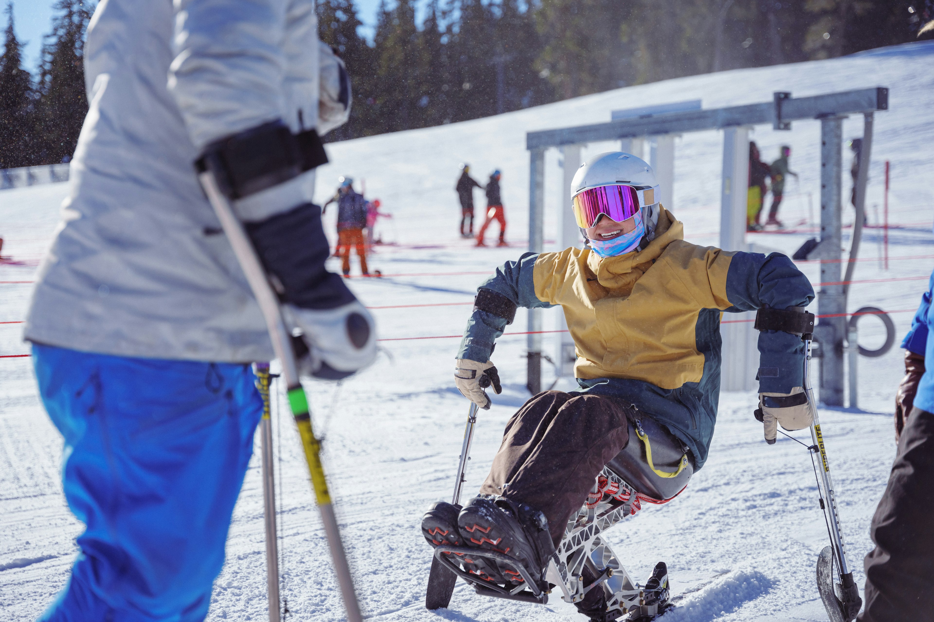 An adaptive athlete who is using a sit-ski smiles and talks with a friend while on a weekend winter ski trip in the Pacific Northwest