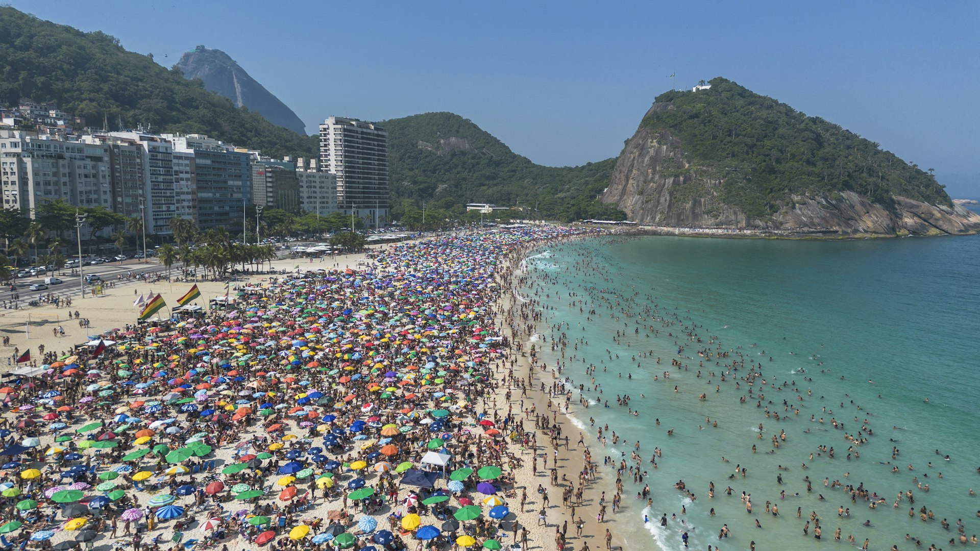 A crowded beach packed with people taking shade under colorful umbrellas