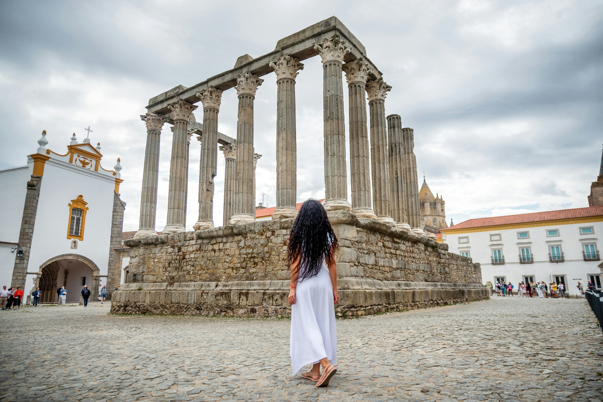 rear view of portuguese woman with white long dress in front of Roman ruins of Diana temple, Evora, Portugal