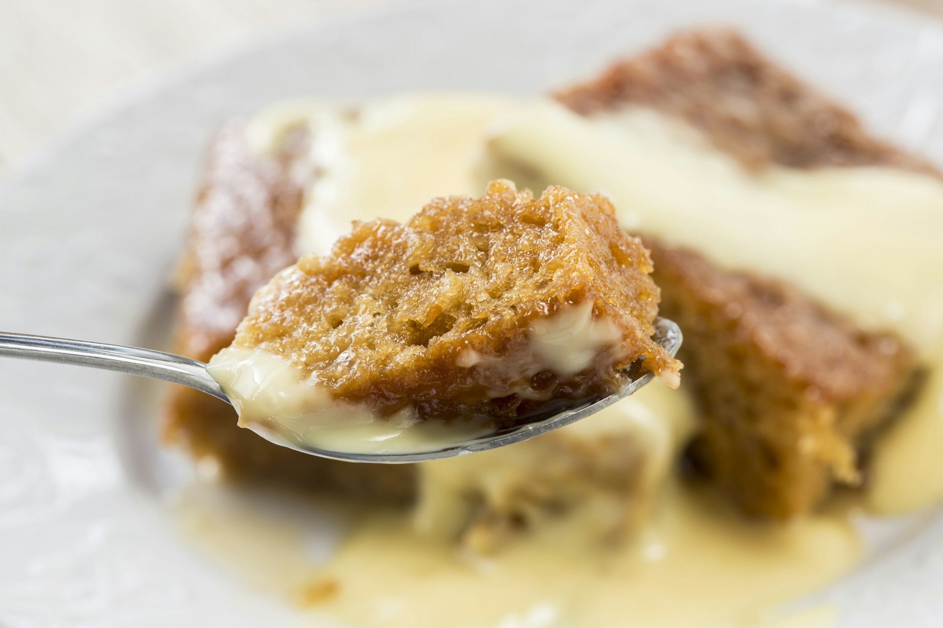 A spoonful of steaming malva pudding on a fork and caped in yellow custard