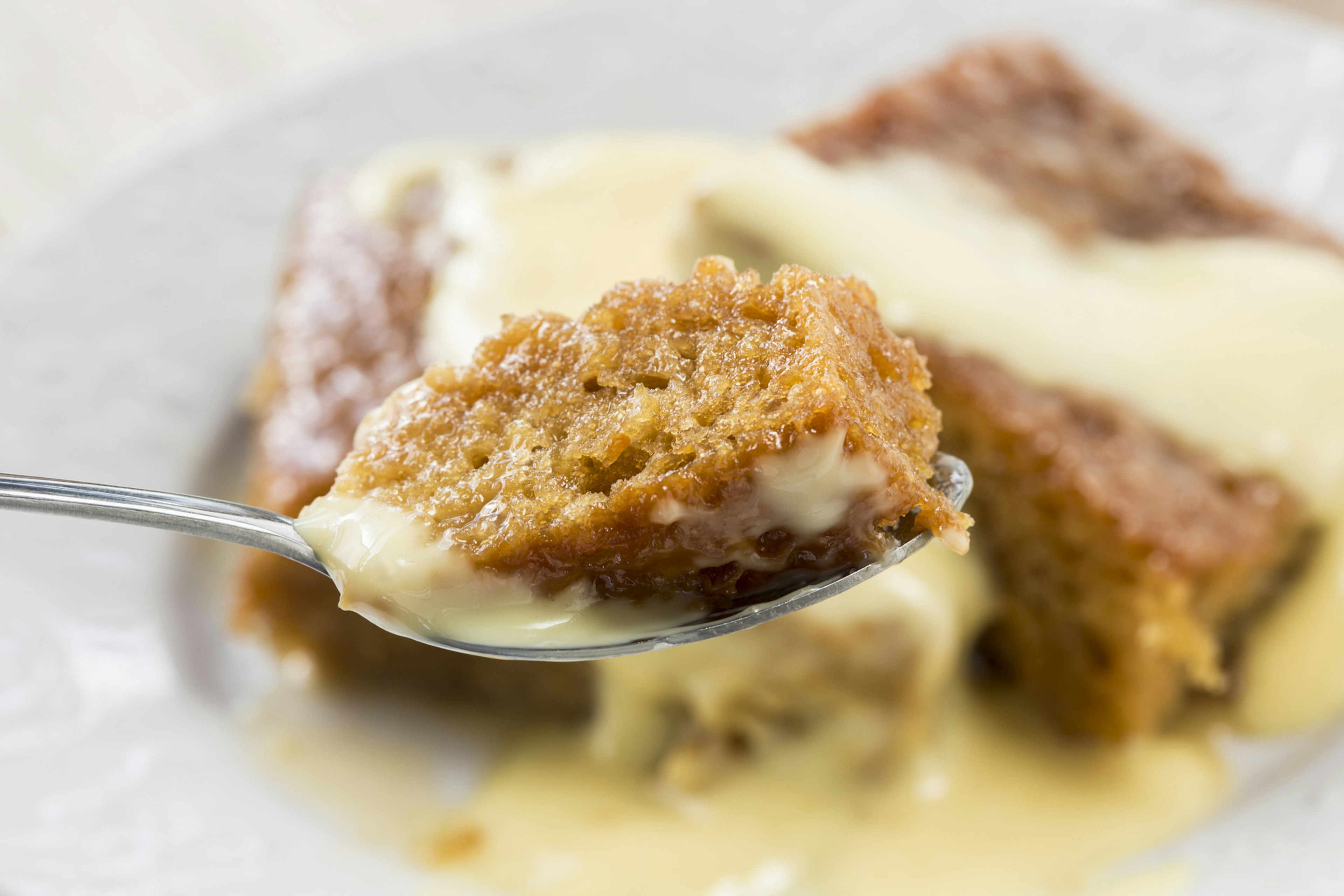 A spoonful of steaming malva pudding on a fork and caped in yellow custard