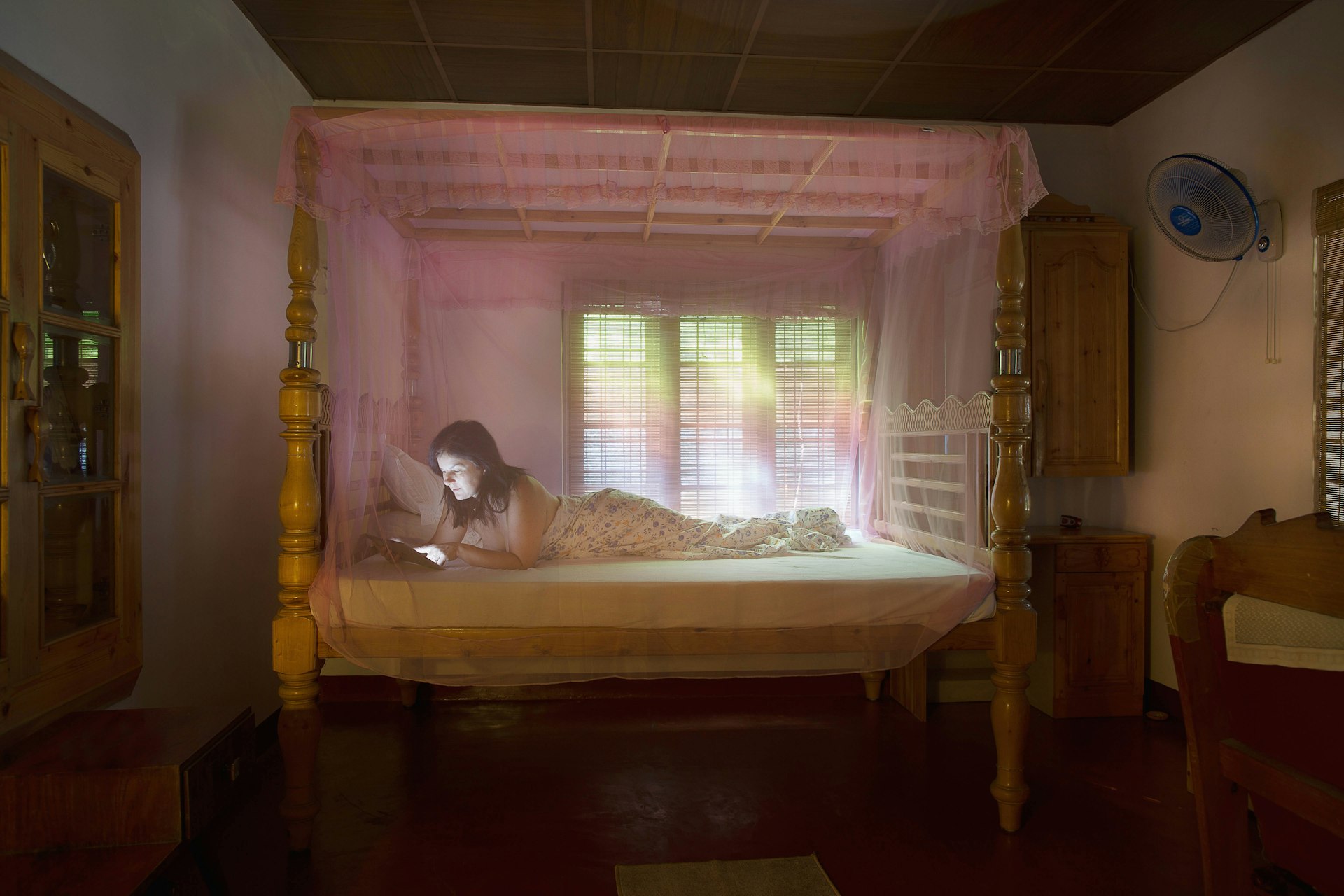 A woman relaxes on her bed beneath a mosquito net