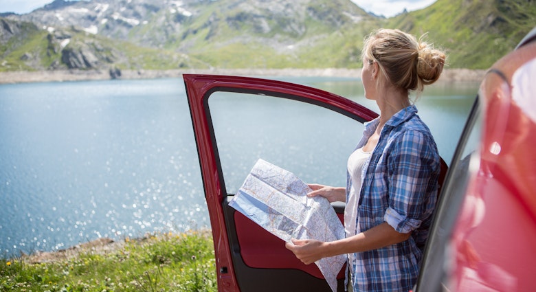 A woman holding a map next to her car with a lake in the background in Switzerland