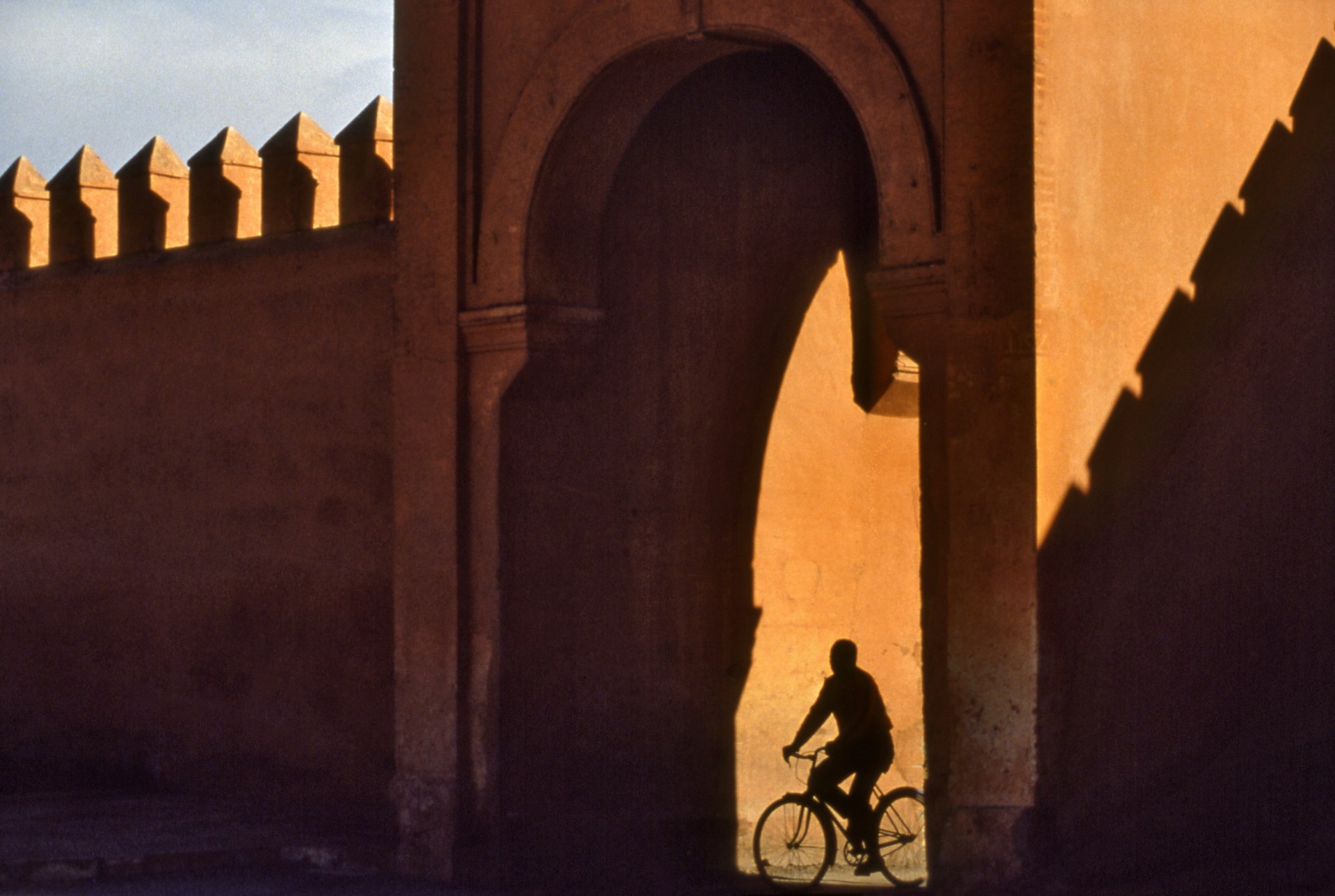 A silhouette of a cyclist passing through a gateway in the red walls of the city