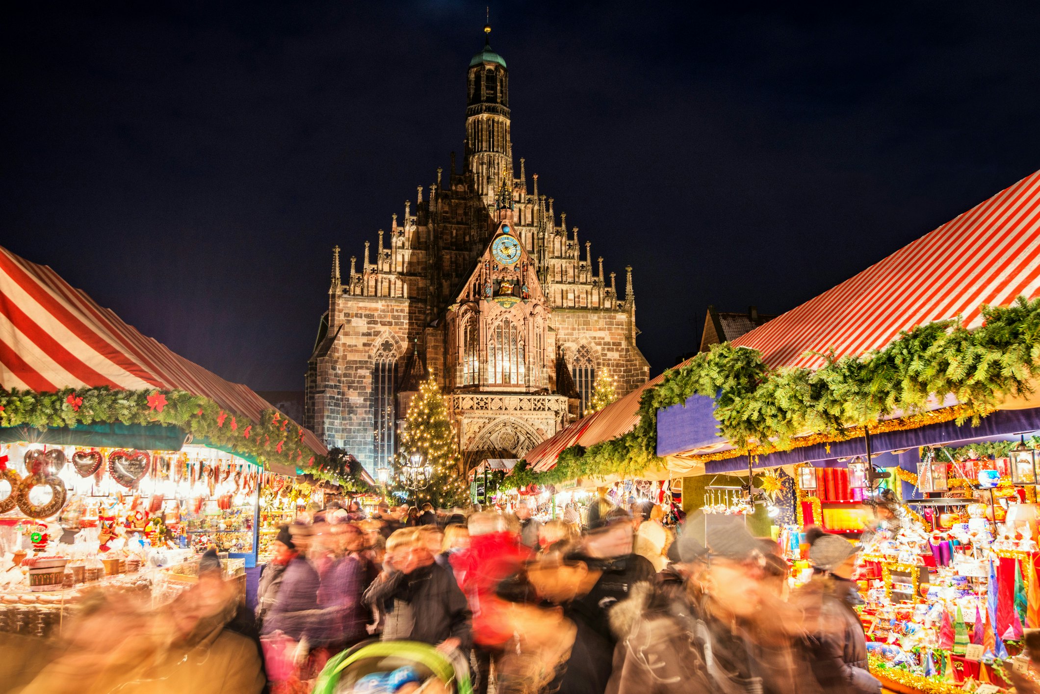 A blurred image of peoples and stalls and lights at a Christmas market with the Frauenkirche church in sharp focus in the background.