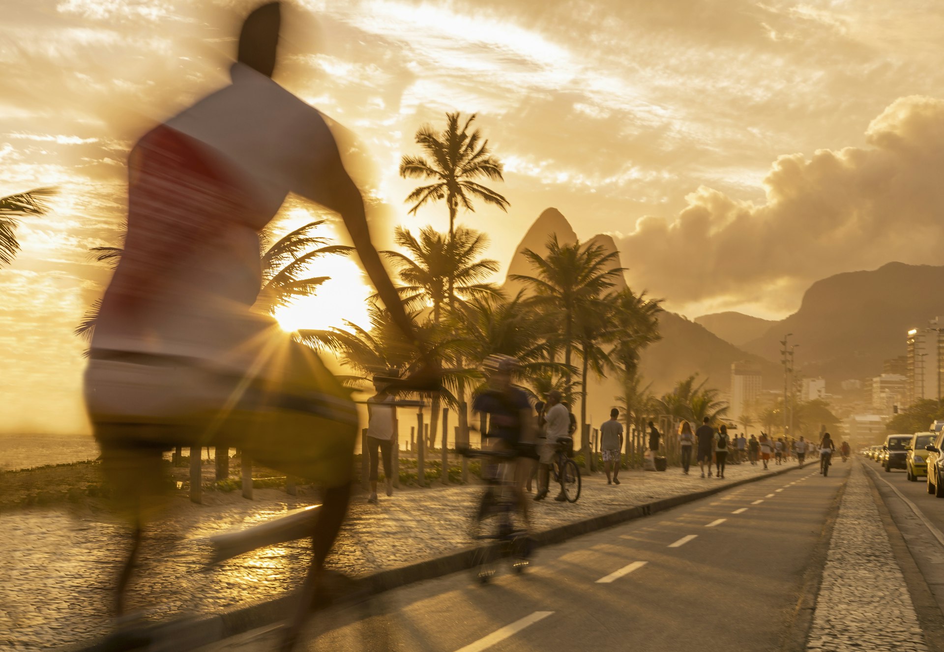 People ride bikes along Ipanema Beach at sunset