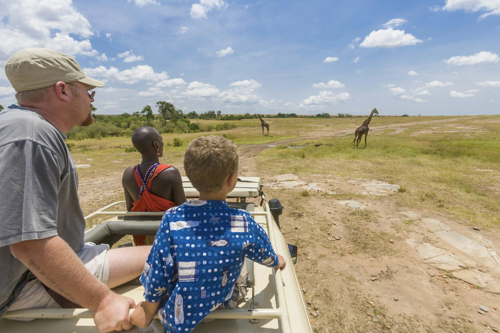 Young boy watches giraffes from a safari vehicle in the Masai Mara, Kenya, East Africa