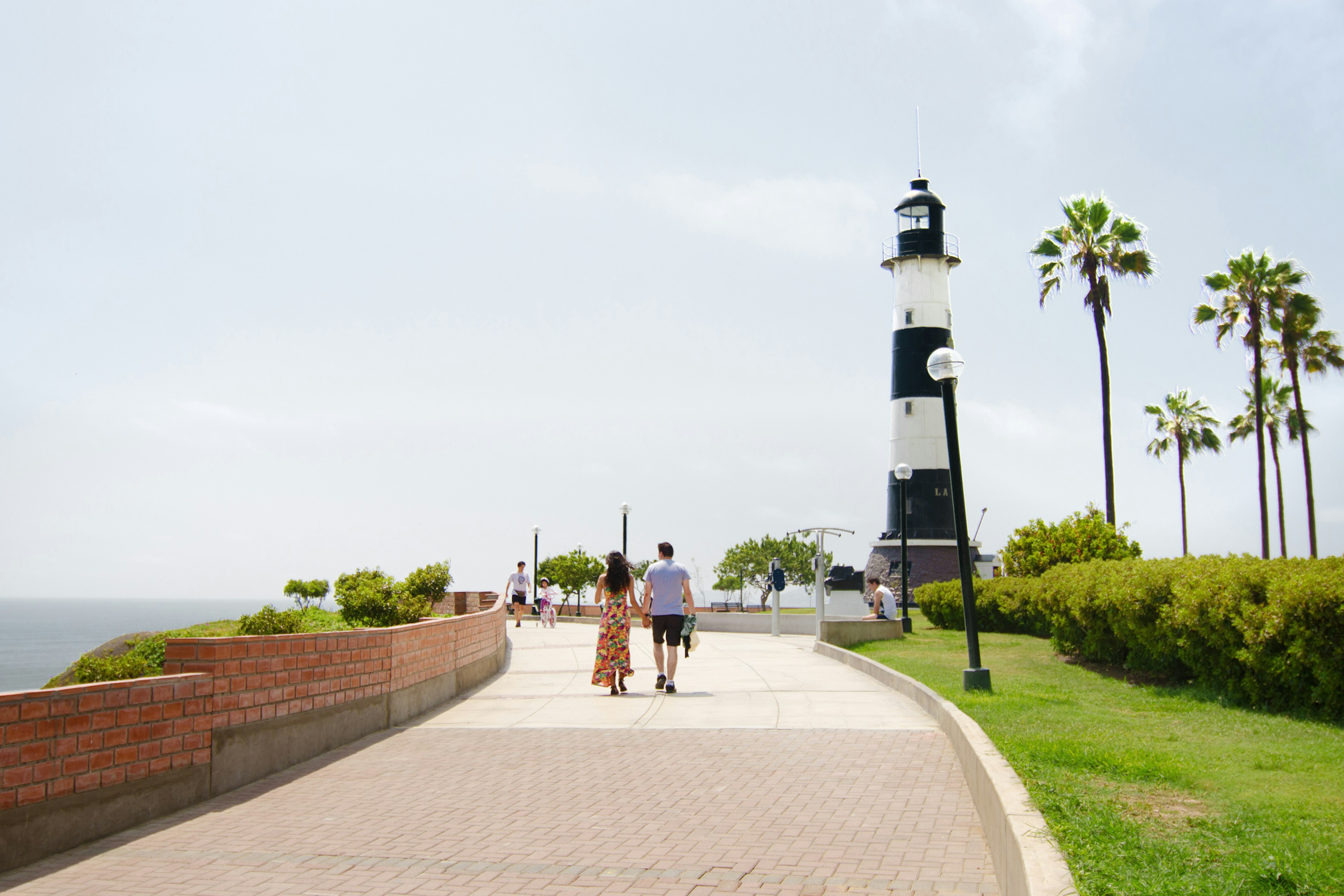 Couple walking on the boardwalk on Lima. Peru towards a black and white lighthouse