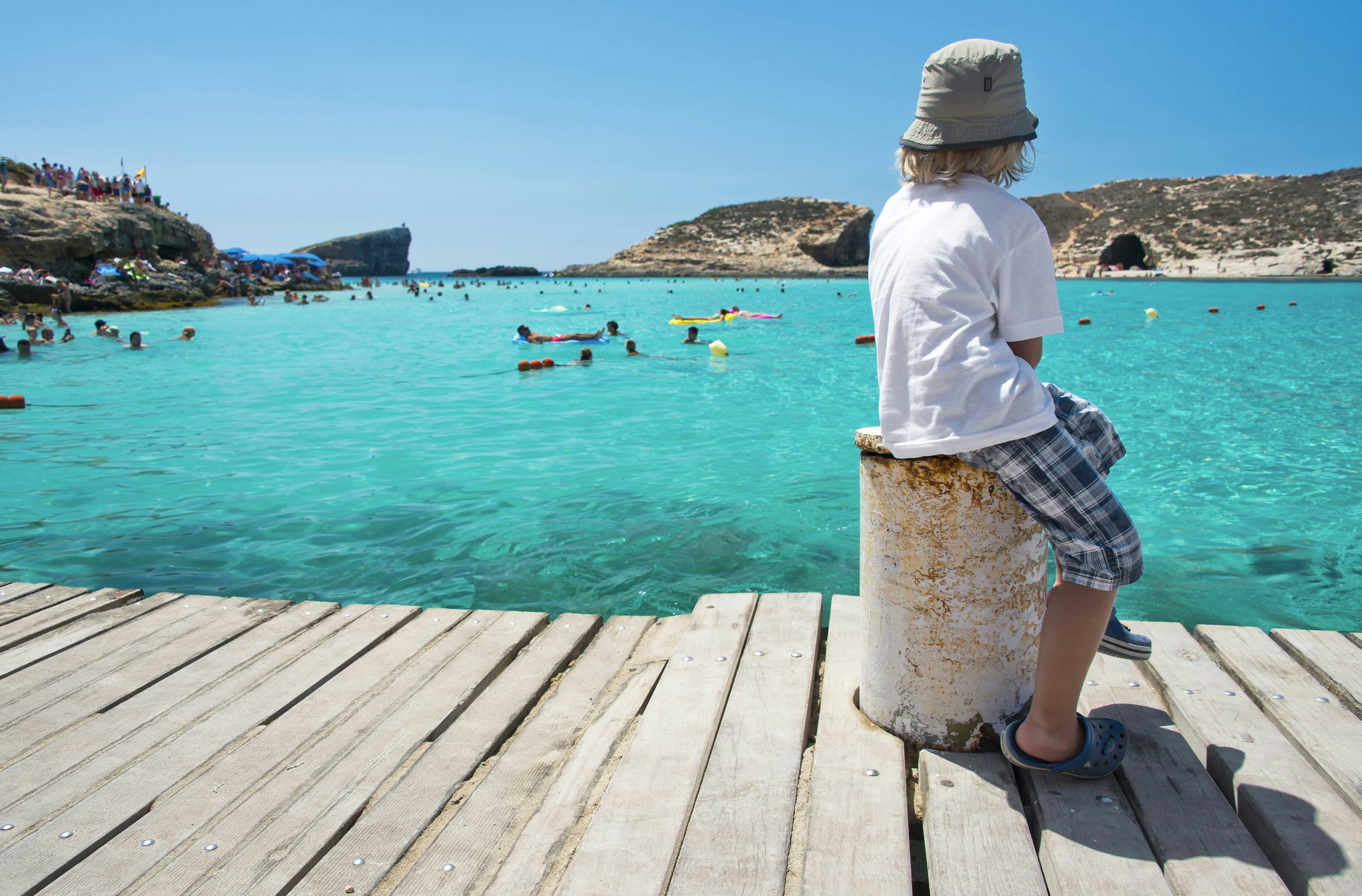 A young child sits at the side of a lagoon looking out at the swimmers