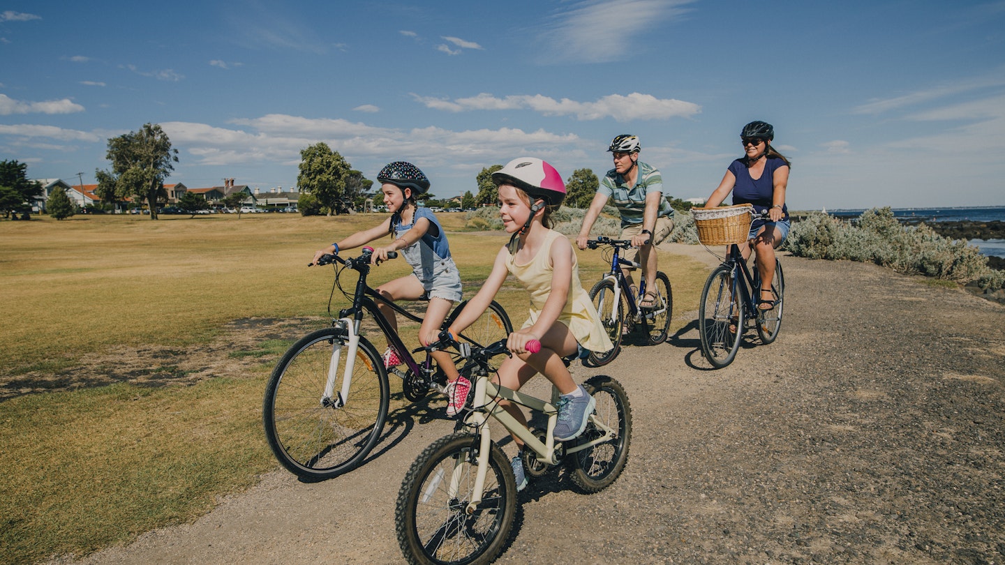 Two parents cycling with their two kids through a park in Melbourne