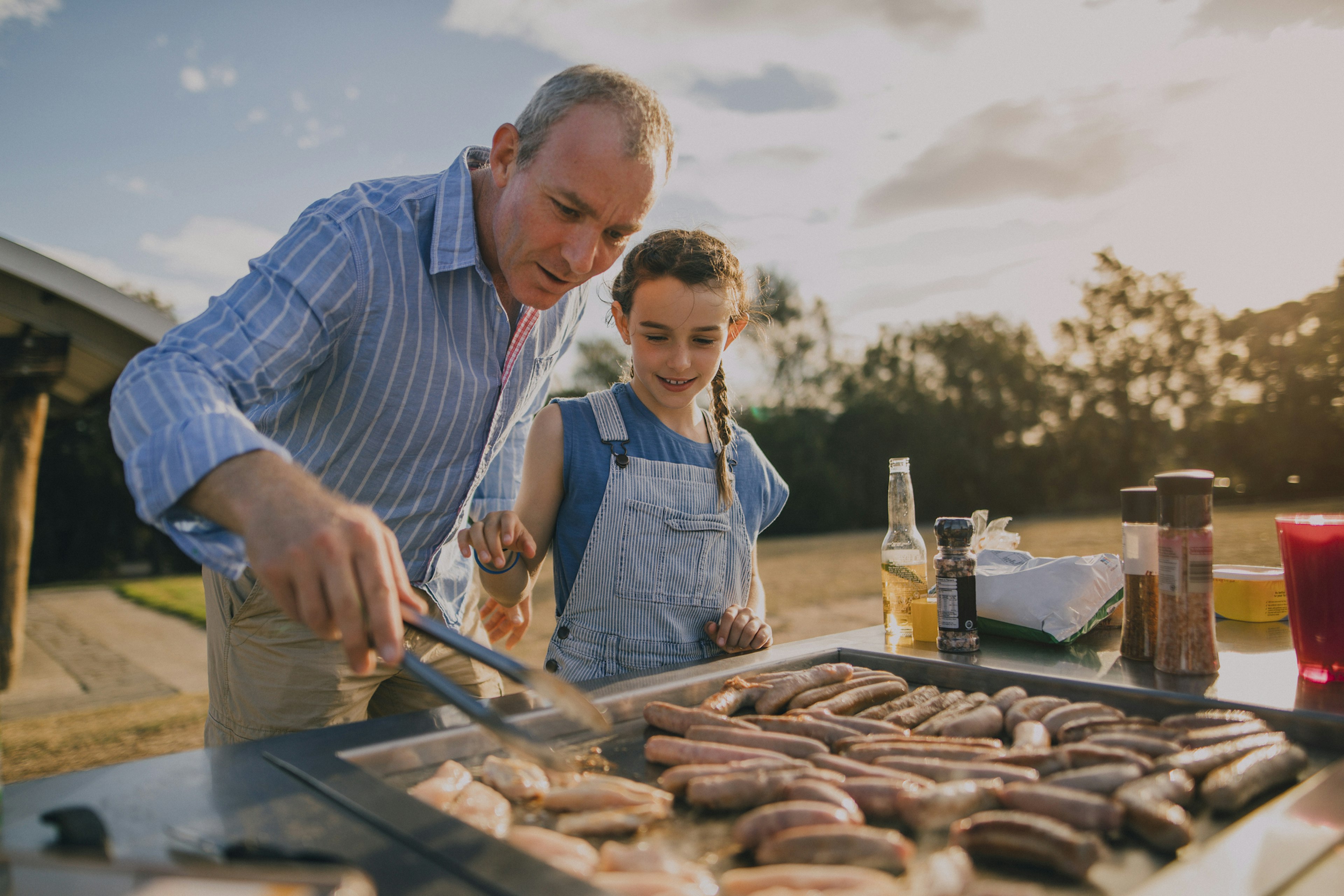 A young girl helping her dad cook on the barbecue in a park in Melbourne