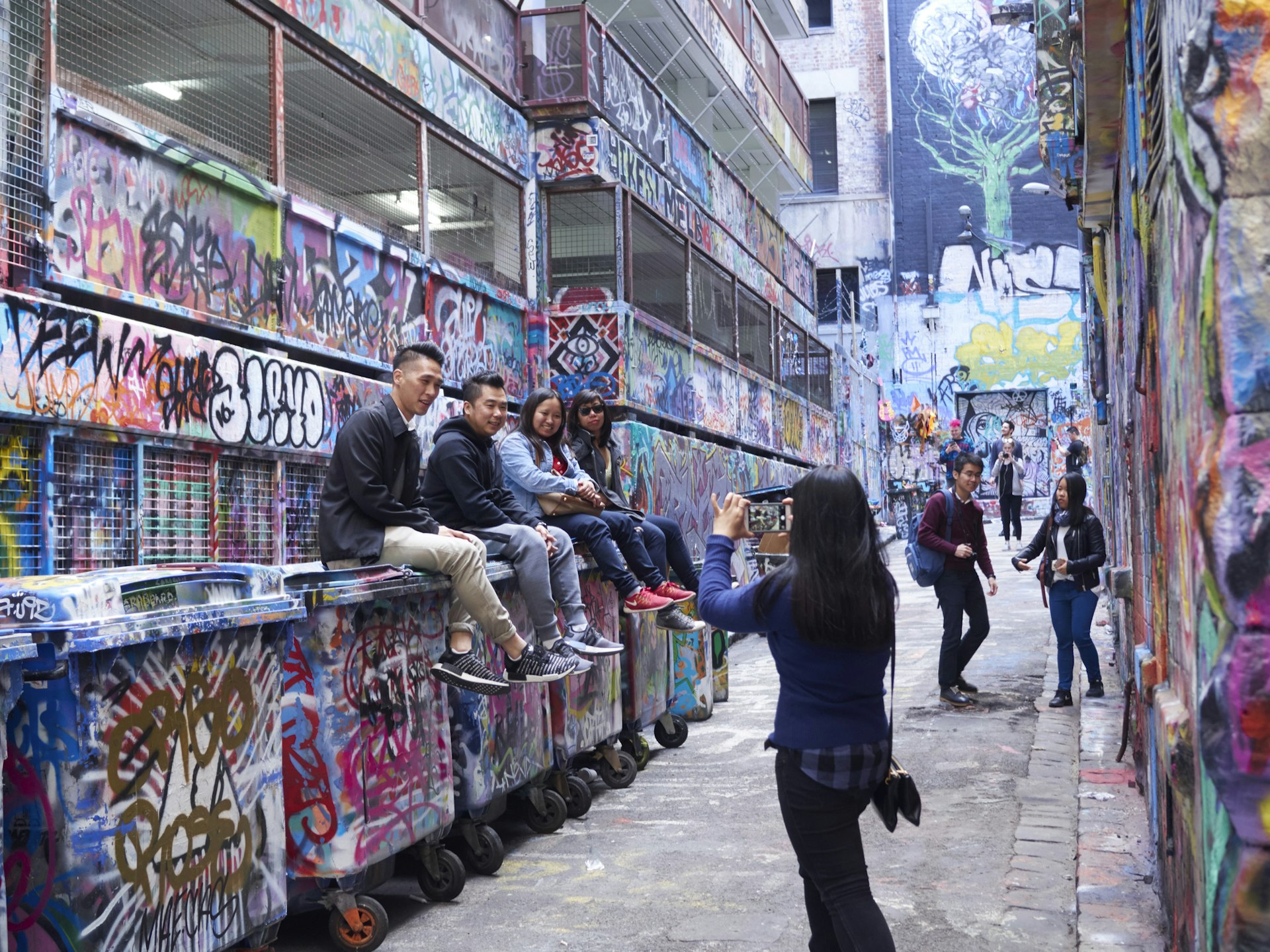 A woman taking pictures of friends in a graffiti-covered lane in Melbourne
