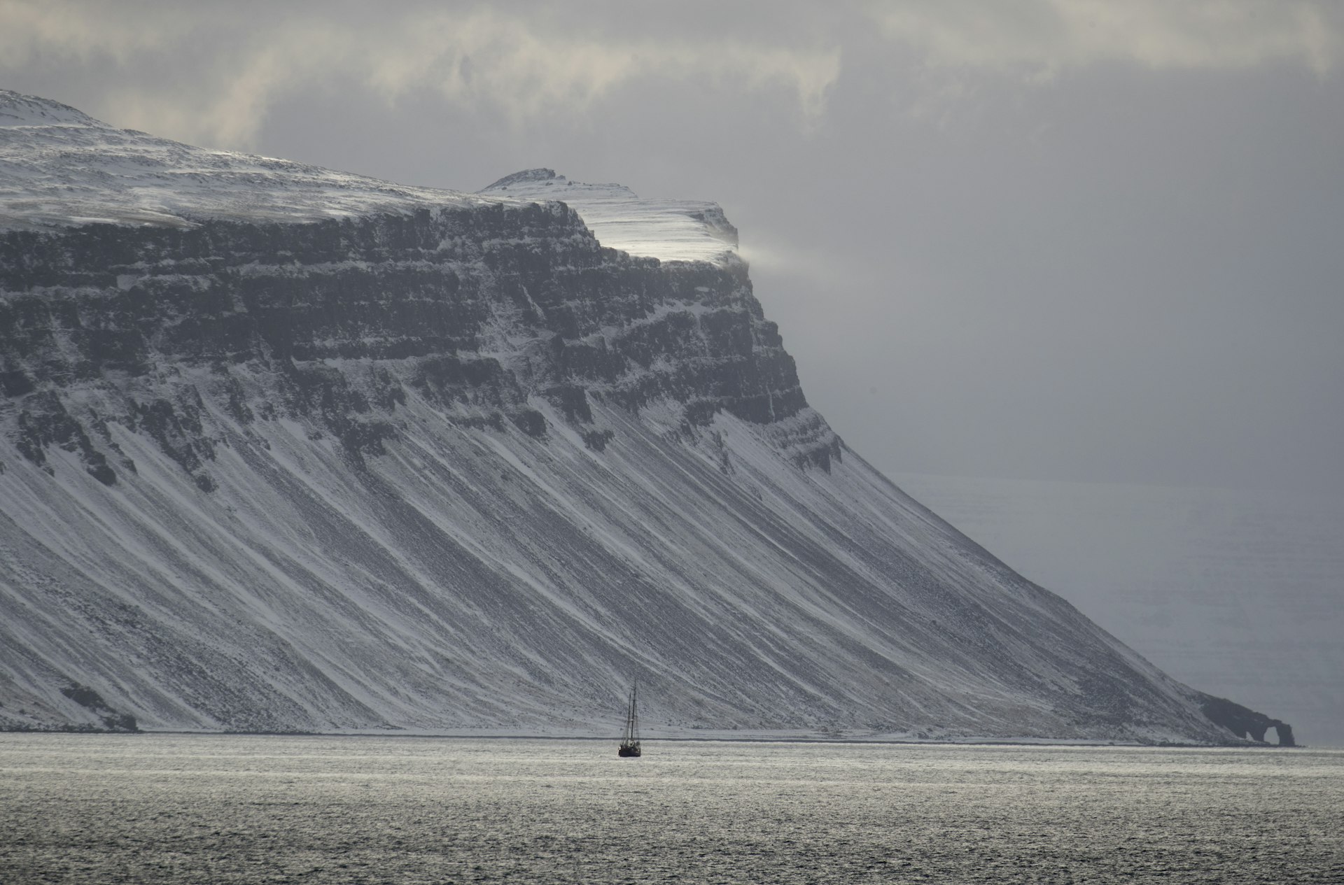 A mountain with a sailing boat out on the water in front of it at Hornstrandir Nature Reserve, Westfjords, Iceland