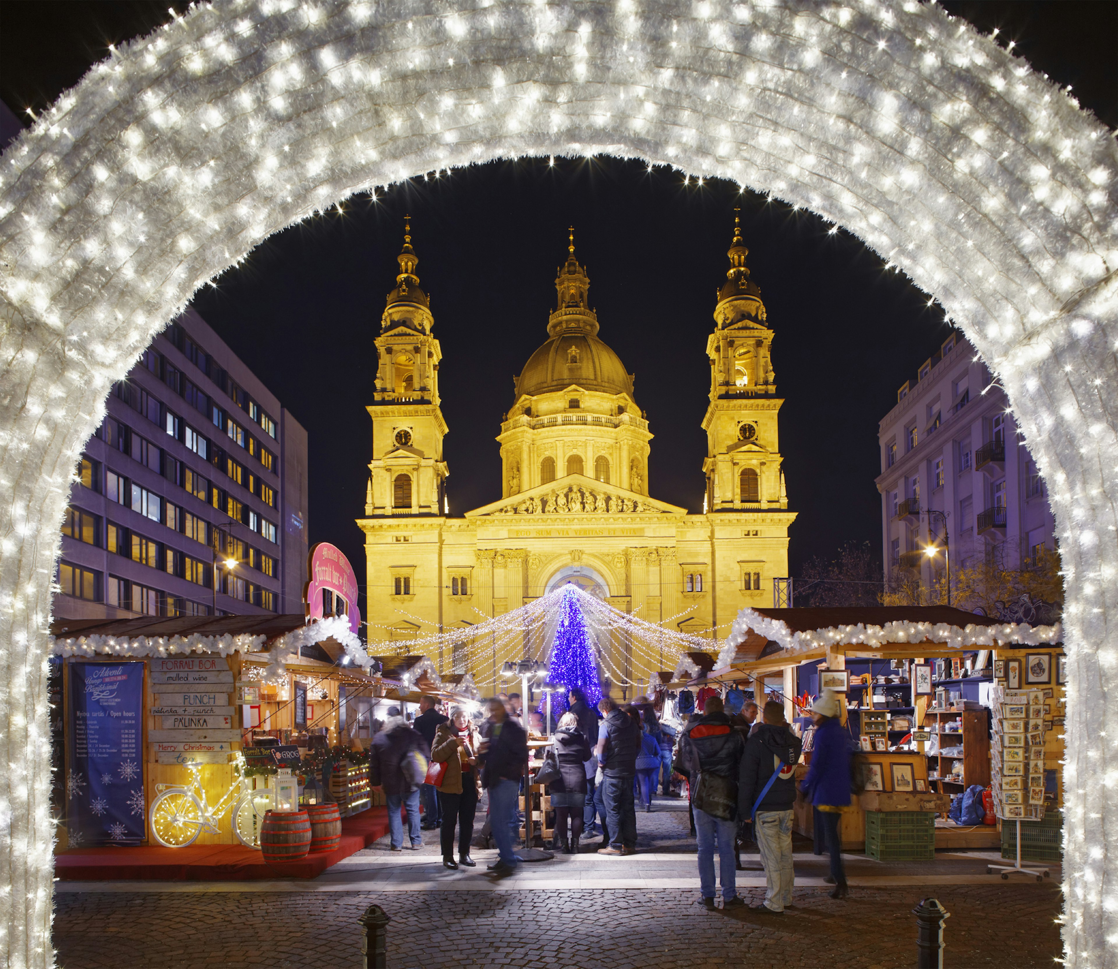 A Christmas market with a neon-blue tree in front of a large basilica