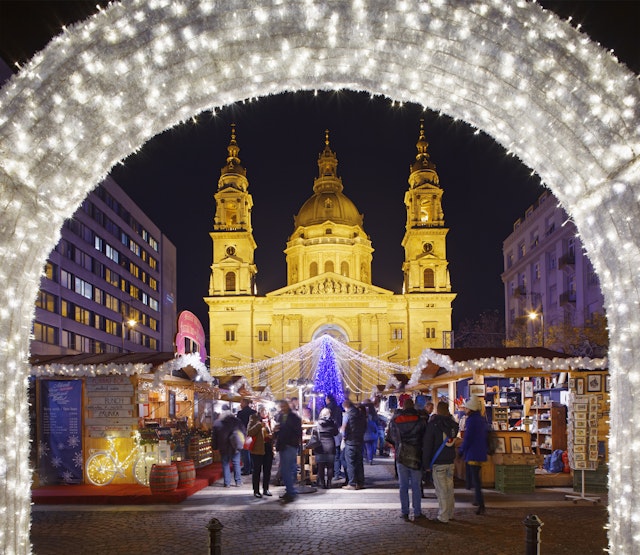 A Christmas market with a neon-blue tree in front of a large basilica