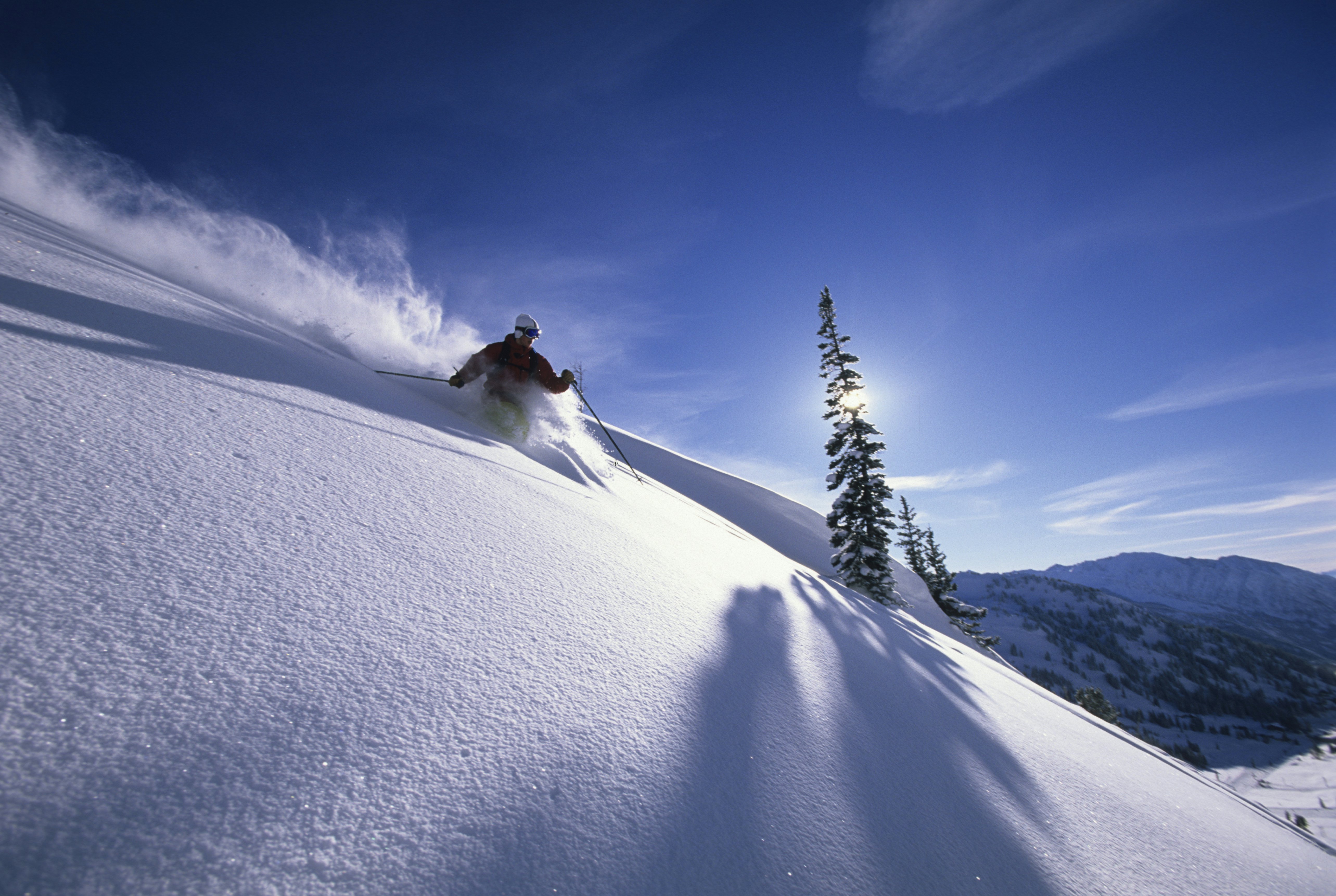 A skier makes a turn on a steep slope, lit by the low rays of the sun.