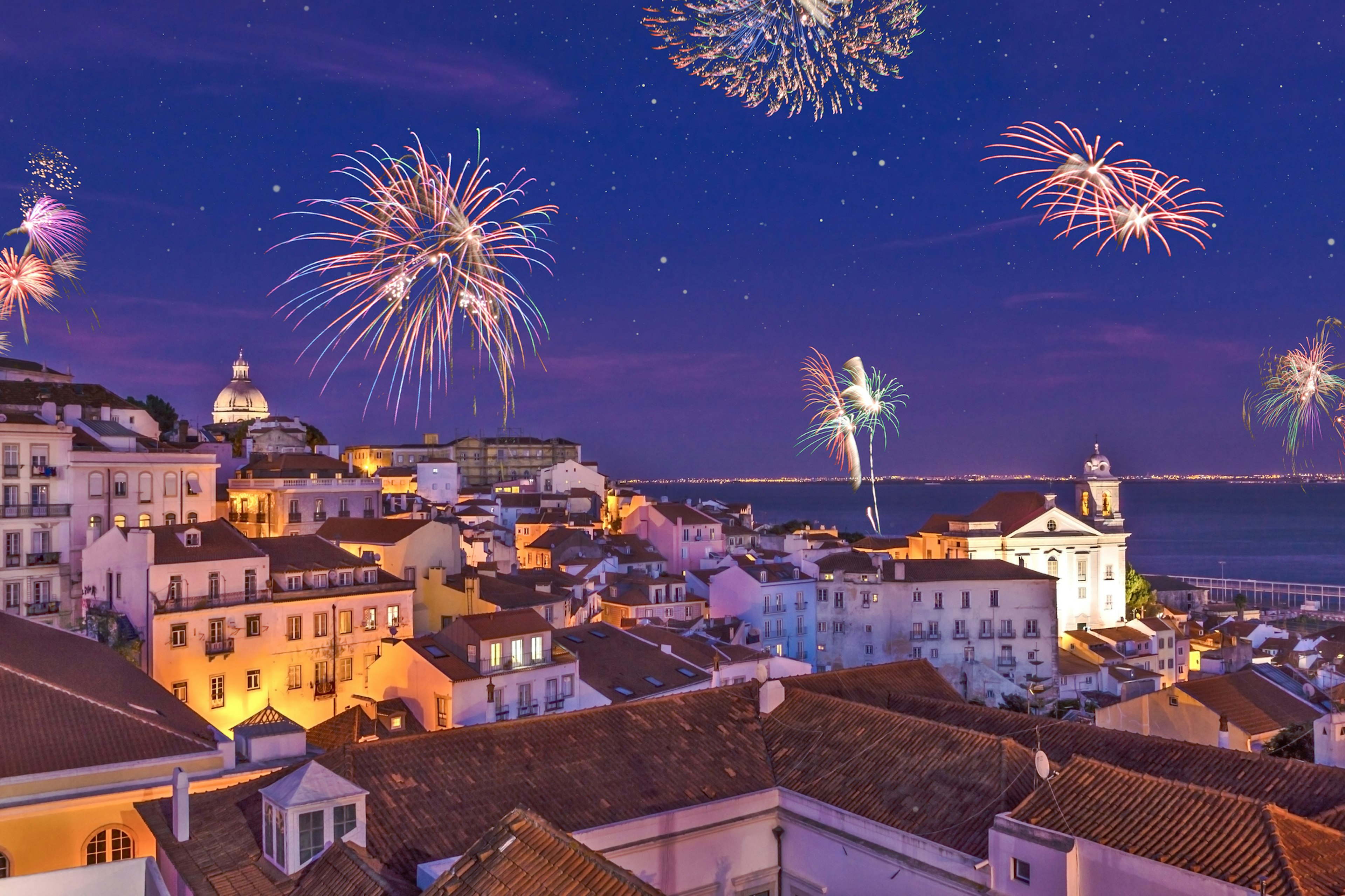 An assembly of fireworks explode above a neighborhood near a river