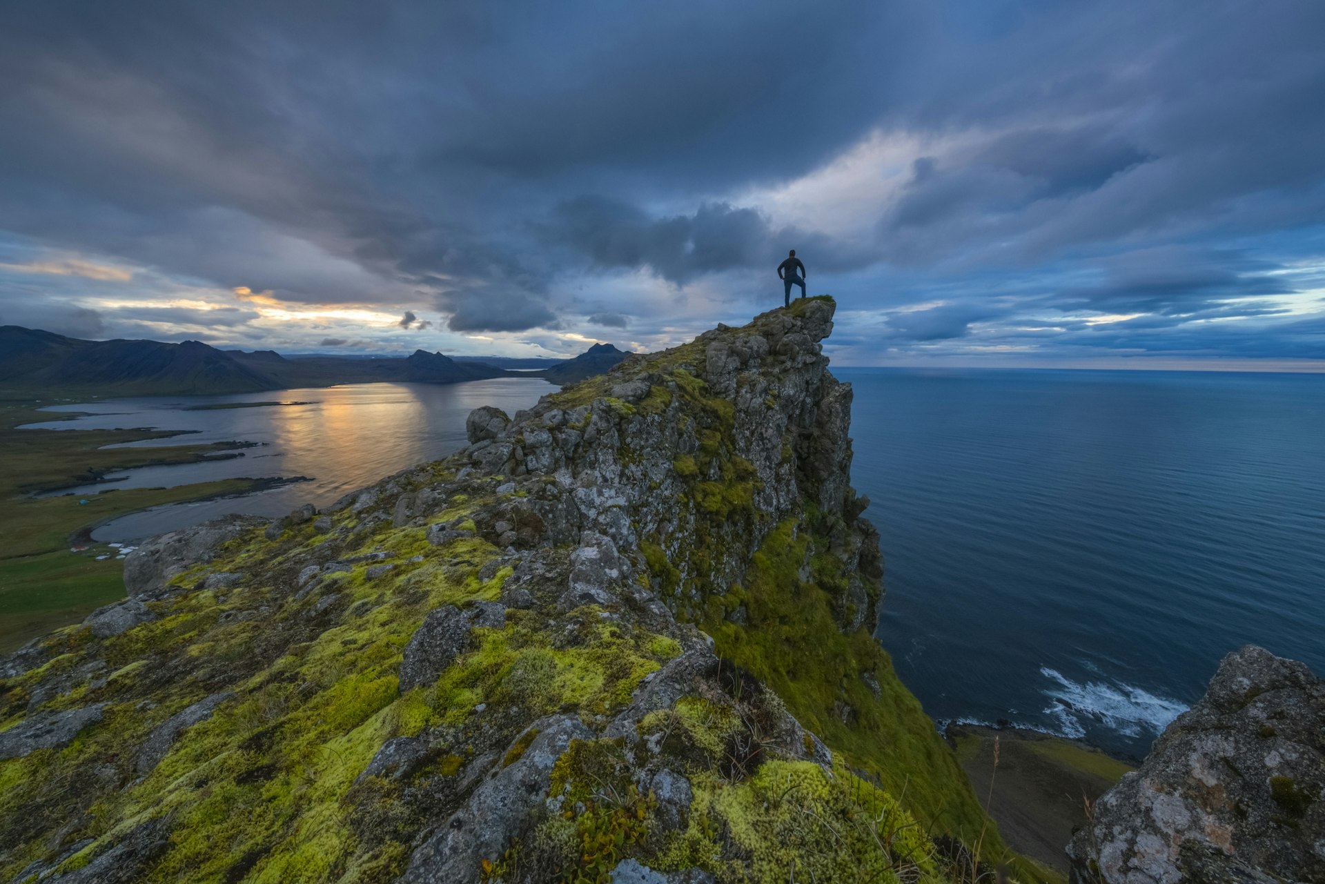 A man stands atop a hill looking out at the waters around the Strandir coast, Iceland