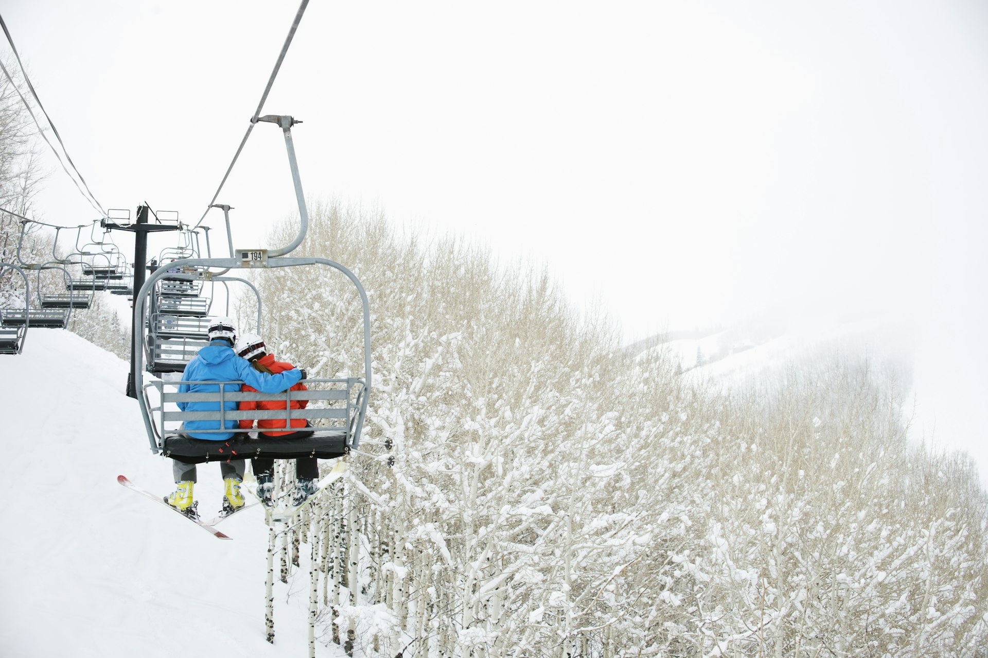 A man with his arm around a skier on a chairlift