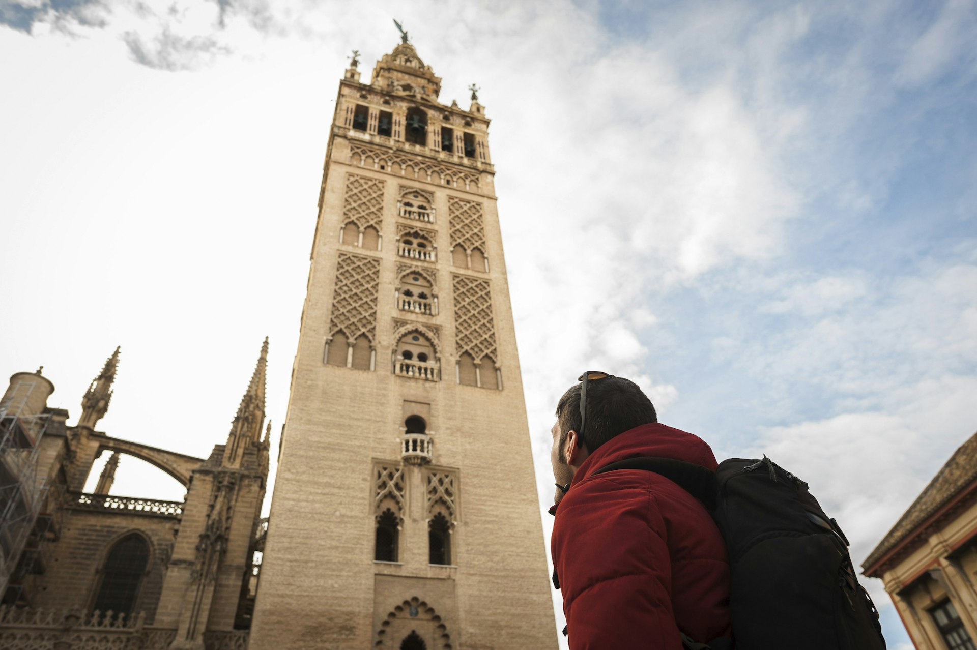Low angle view of backpacker looking at La Giralda in Seville Cathedral against cloudy sky in cit