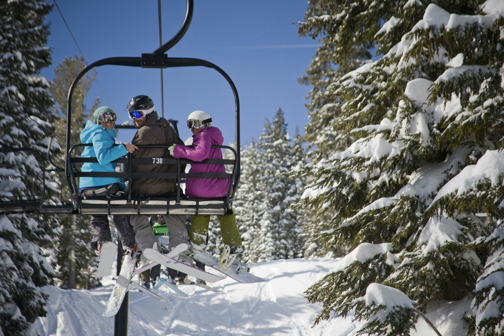 Three smiling skiers on a chair lift during a sunny day in Palisades Tahoe (Squaw Valley), California, USA