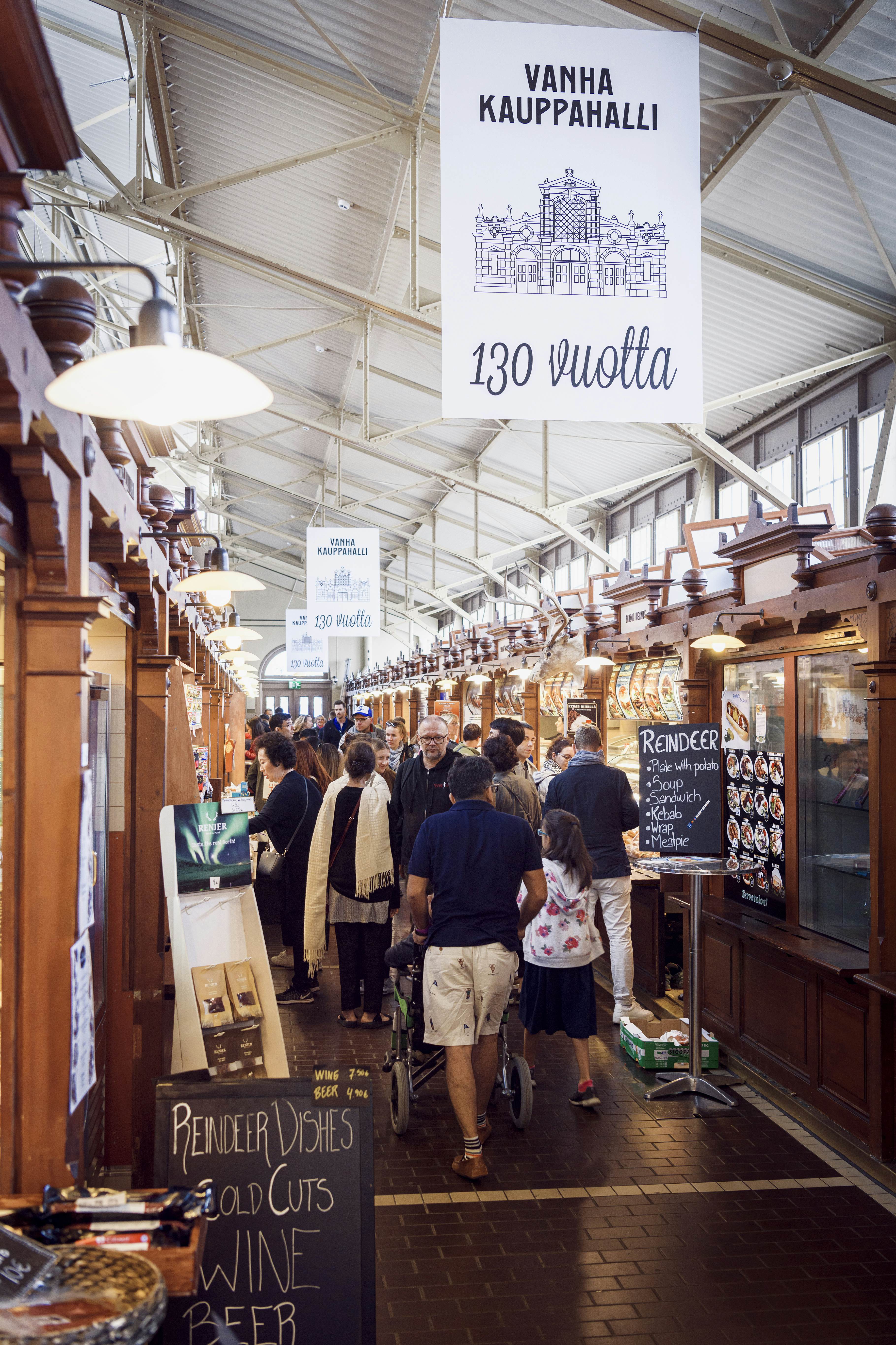 People walk past wooden stalls in a market hall in Helsinki.