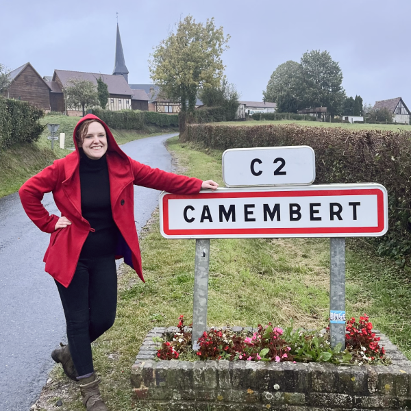 AnneMarie stands next to a town sign that says ''Camembert''