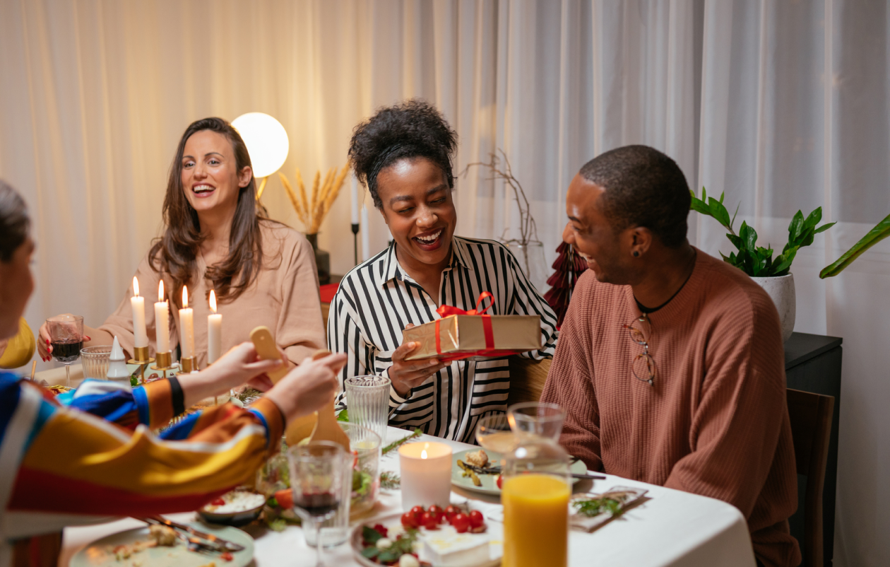 People sitting around the table during the holidays passing presents and eating.