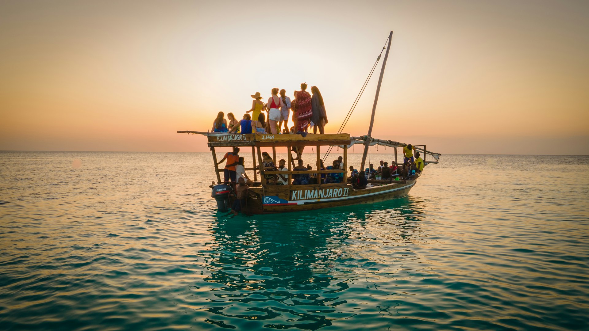 A traditional Dhow with tourists inside and on the roof, on the water at sunset, Zanzibar