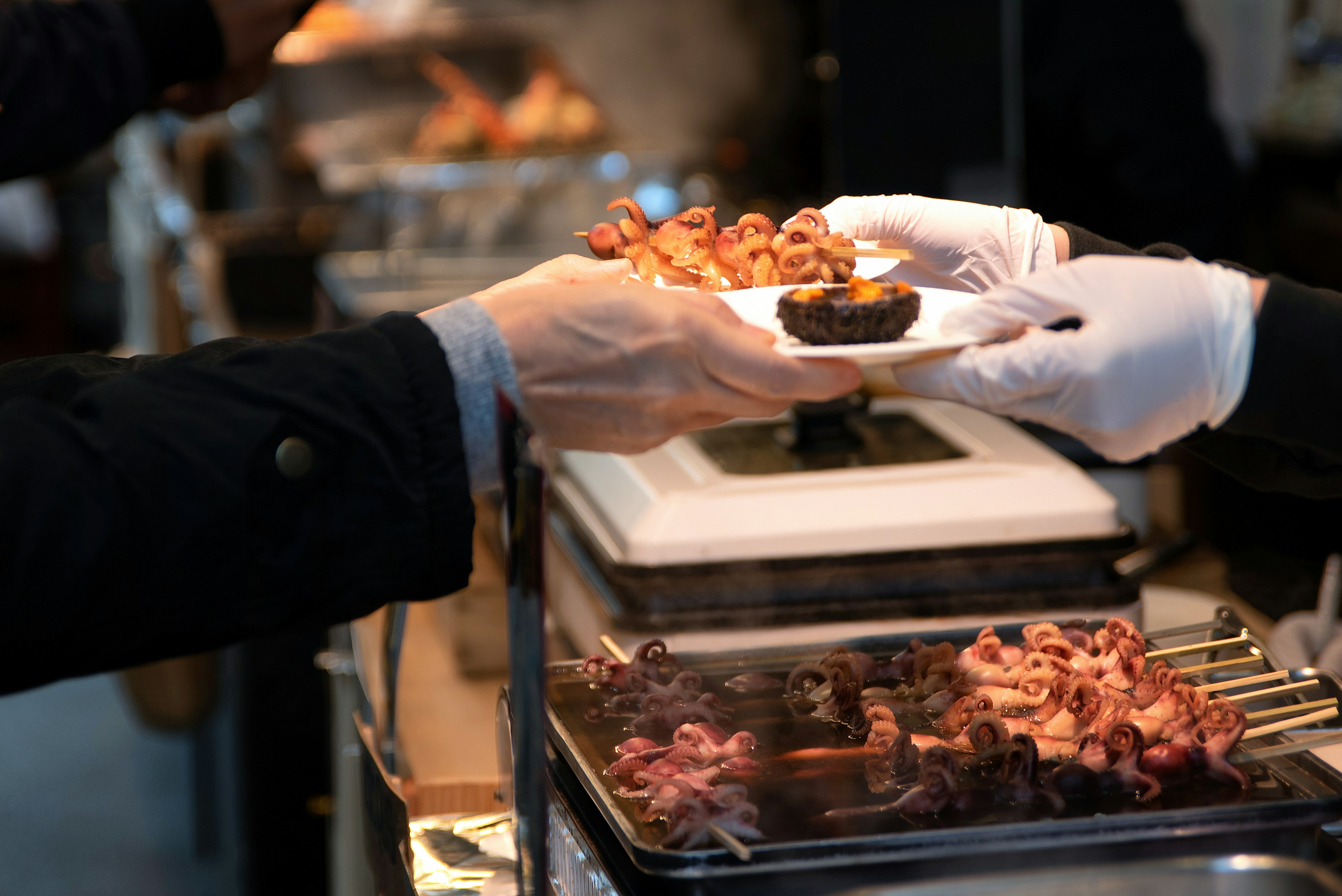 A vendor hands a man grilled baby octopus and uni on a plate