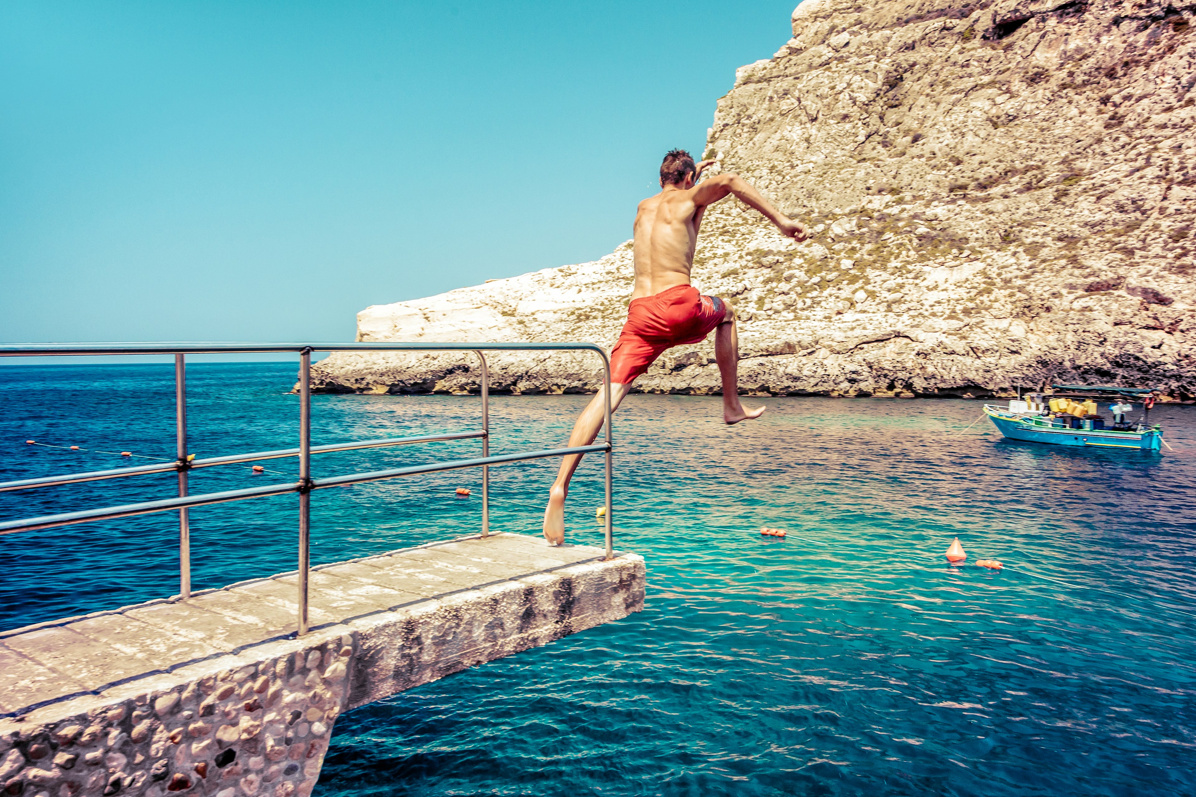 A young man jumps from a walkway into to the sea at Xlendi Beach on Gozo island, Malta