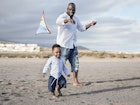 A toddler and his dad playing on the beach with a kite in Africa