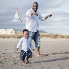 A toddler and his dad playing on the beach with a kite in Africa