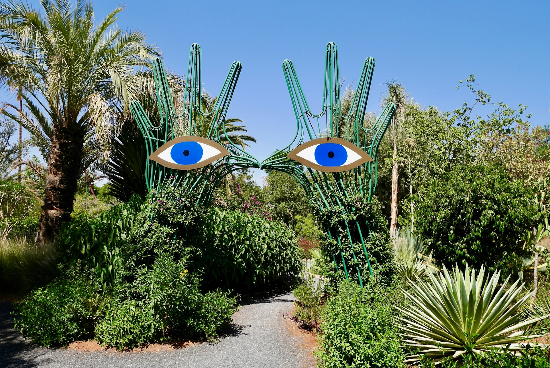 Two large hand sculptures topped with blue eyes guard a pathway in a botanical garden
