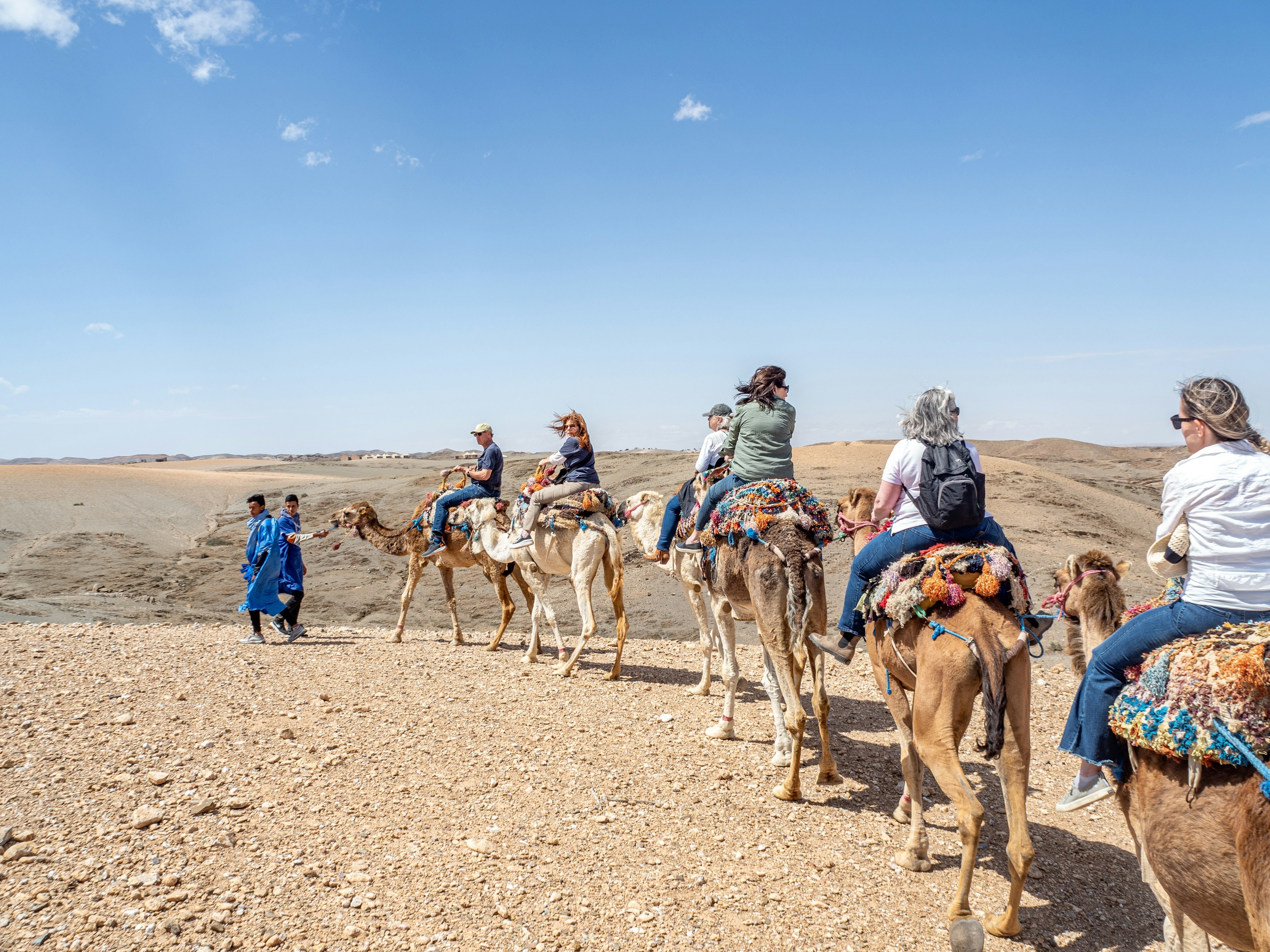 A row of camels with riders makes its way through a desert