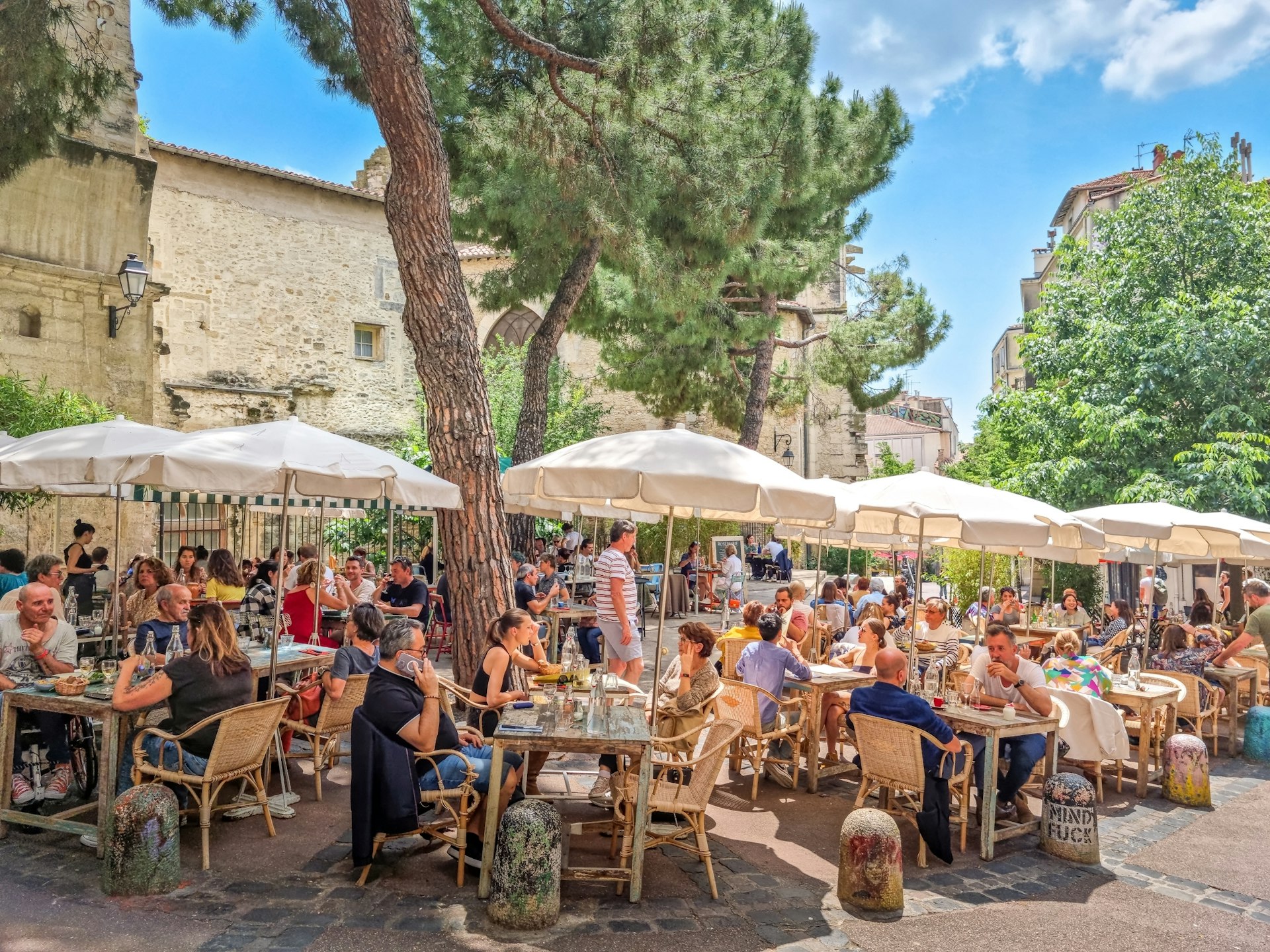 People sit at outdoors tables shaded by trees in a city square