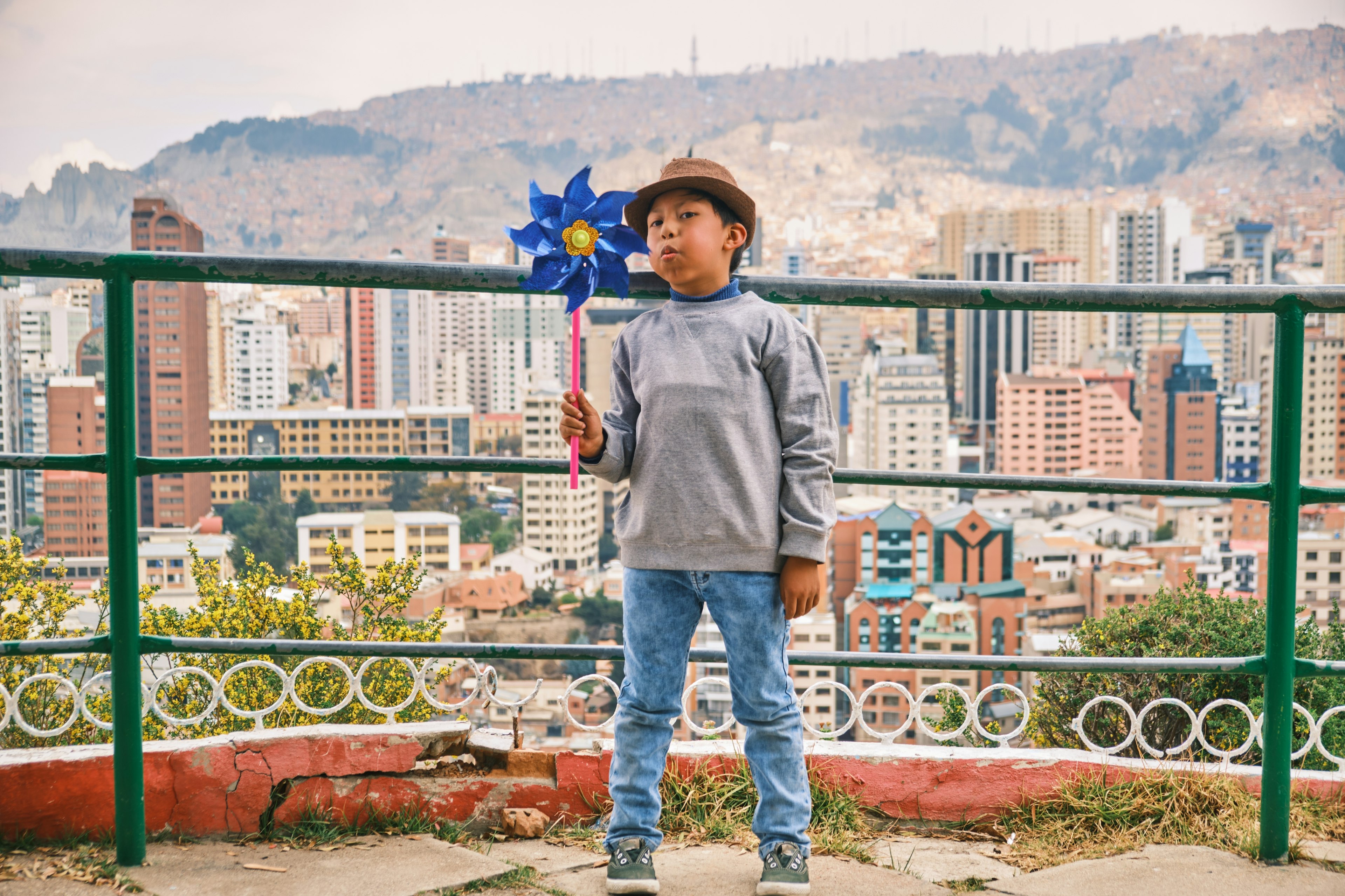 A boy wearing a hat blows a pinwheel windmill in a city