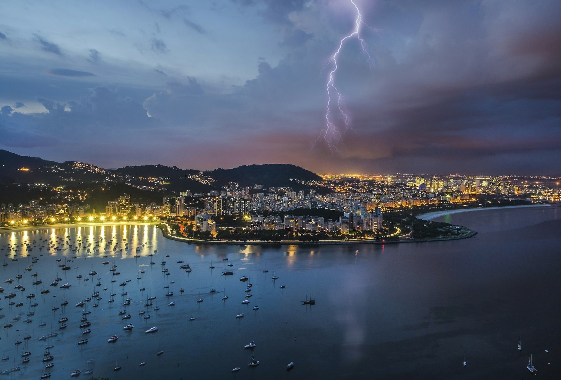 A fork of lightning shoots out of a dark thunderous sky over a coastal city