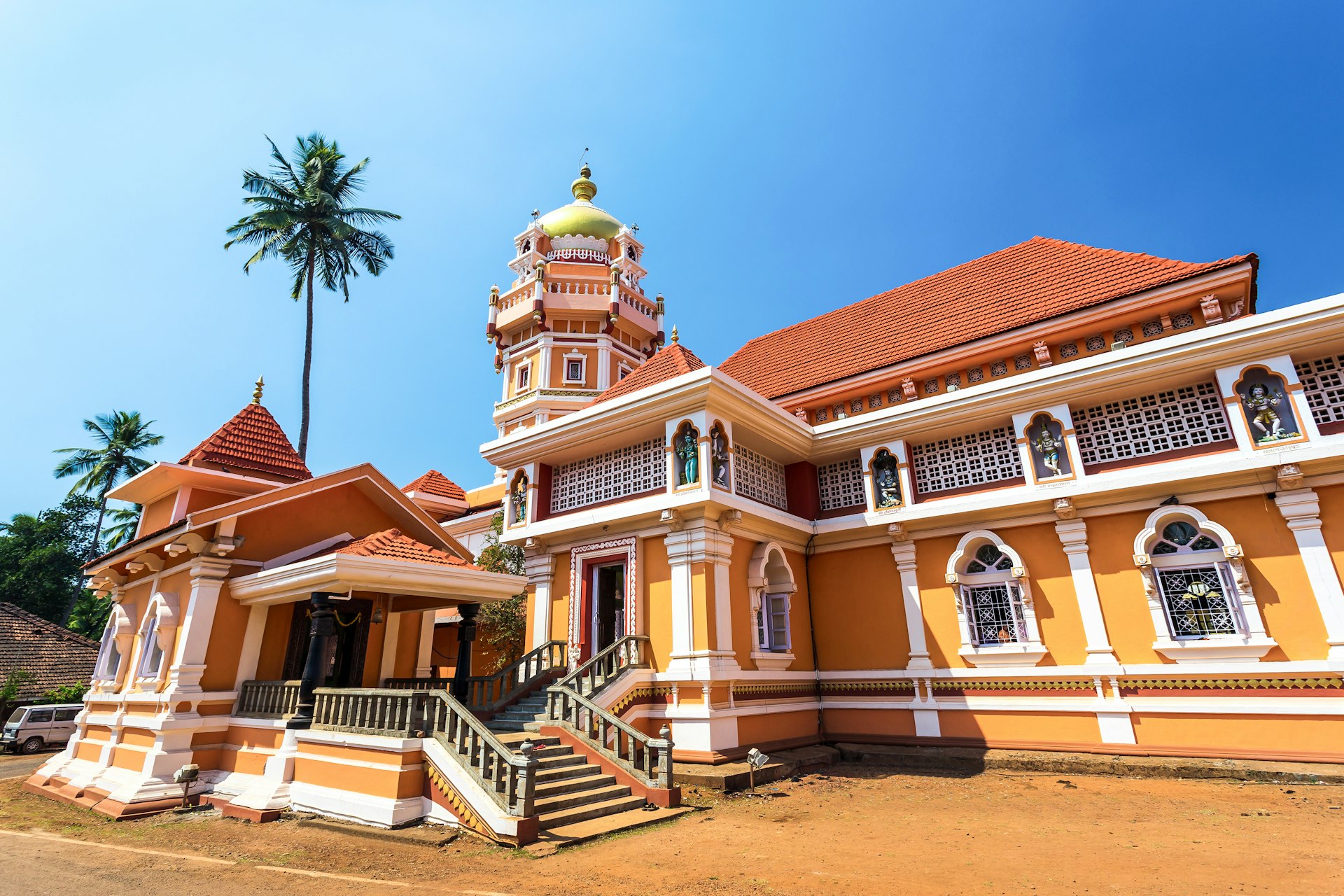 Shree Shantadurga Temple in Goa, India, painted in vibrant yellow-orange against a clear blue sky.