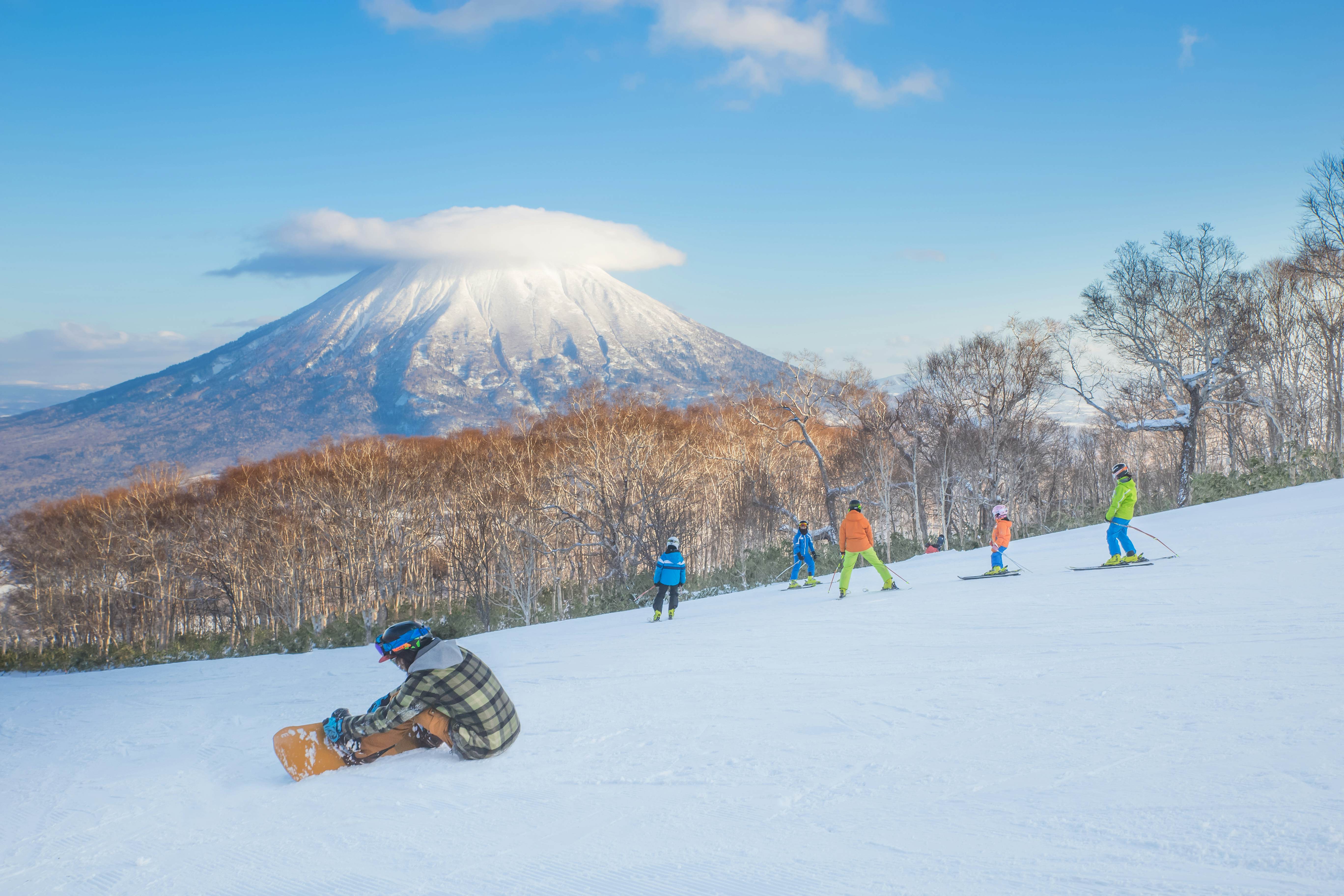 Snowboarders and skiiers on slopes in the shadow of a large mountain peak