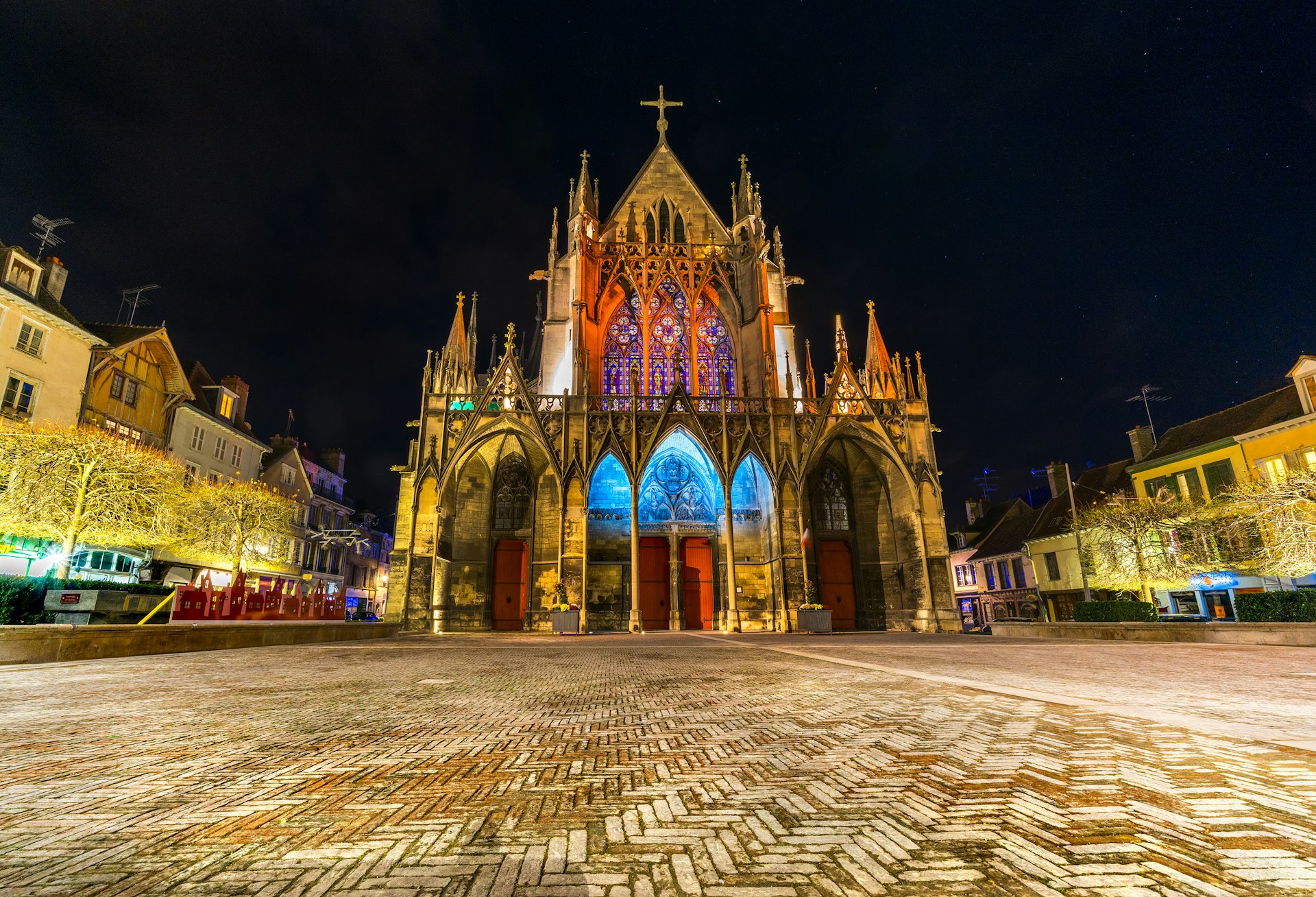Gothic exterior of a basilica on the edge of a square all lit up at night