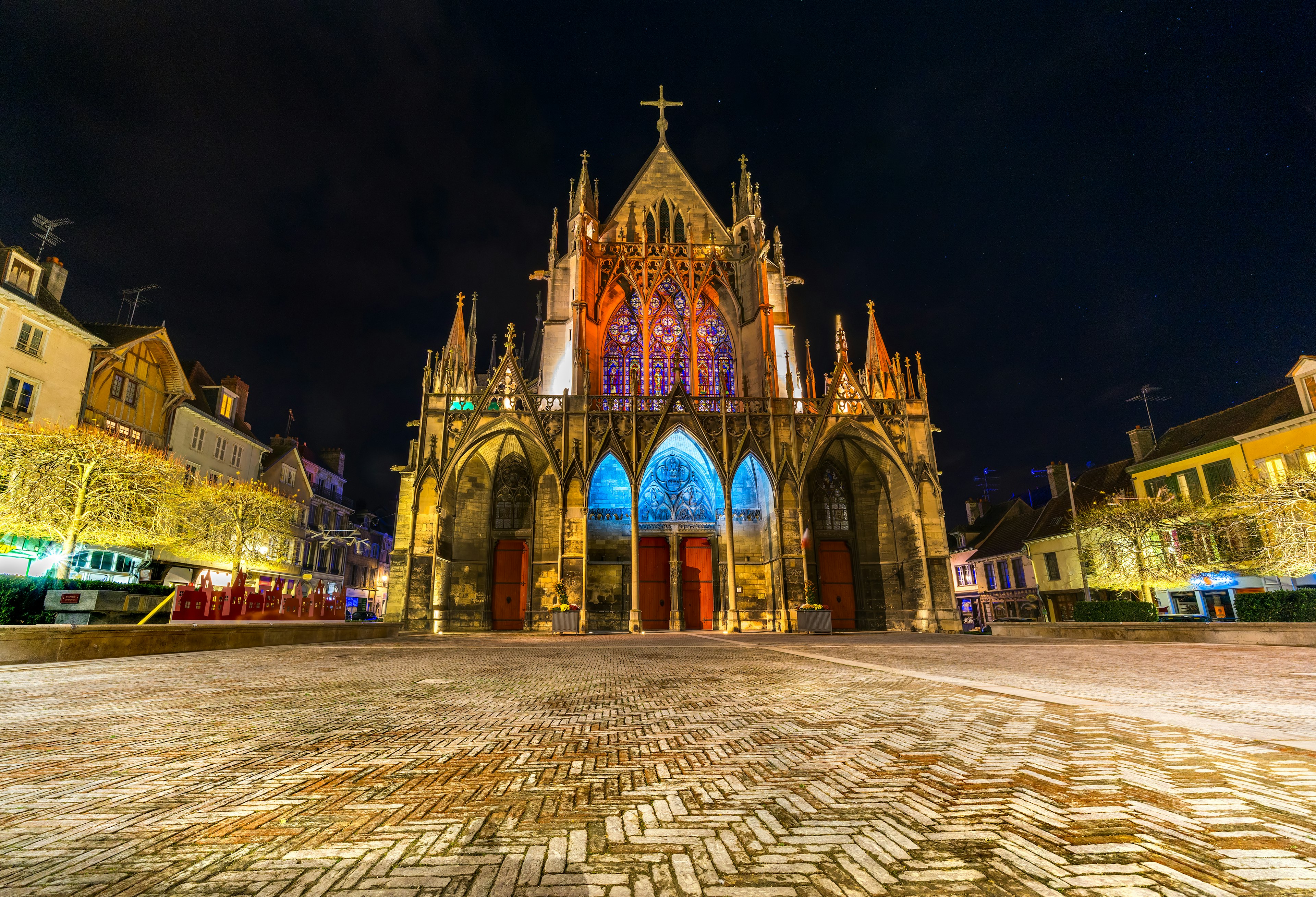 Gothic exterior of a basilica on the edge of a square all lit up at night